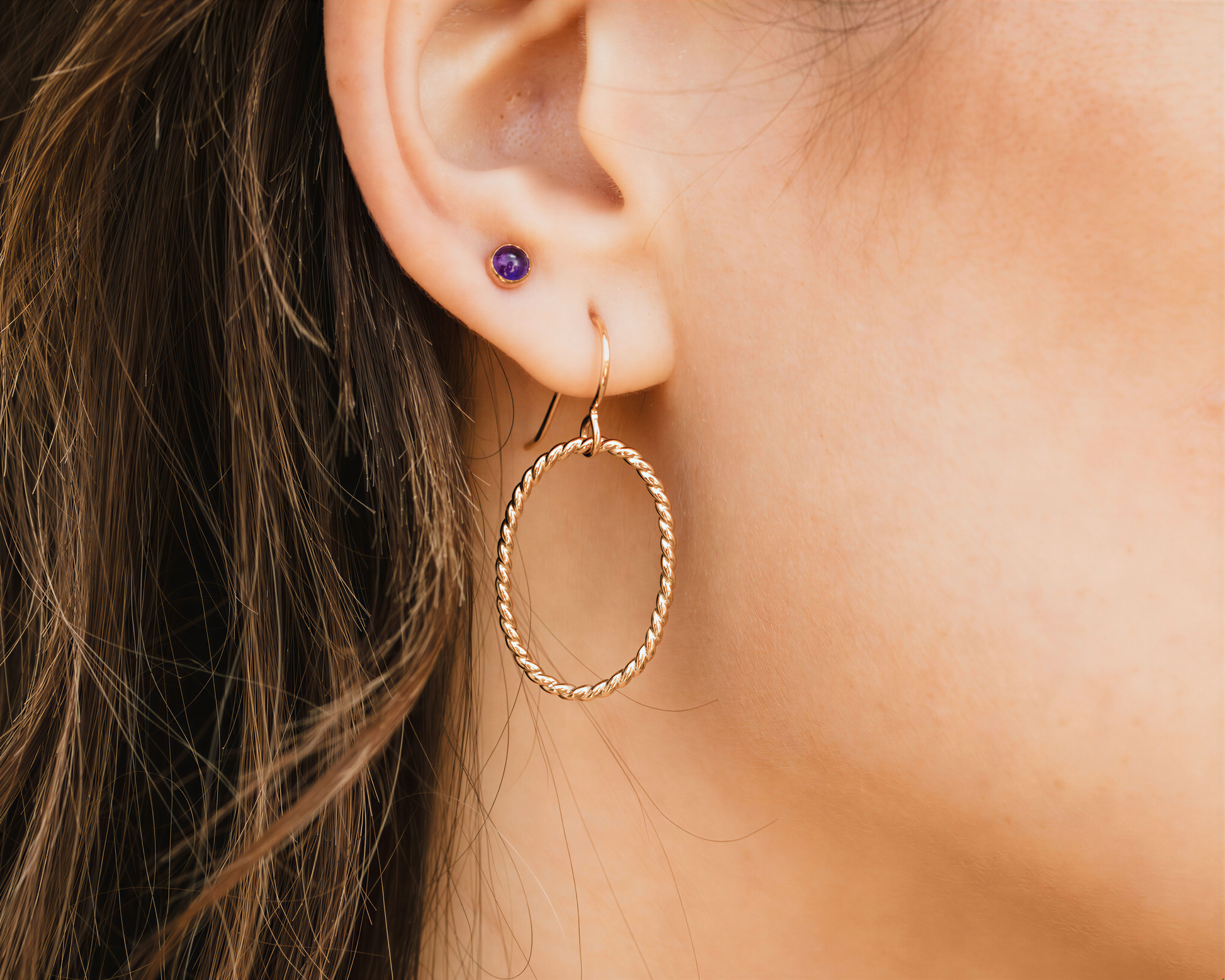 A close-up view of a person's ear adorned with a gold hoop earring and a purple gemstone.