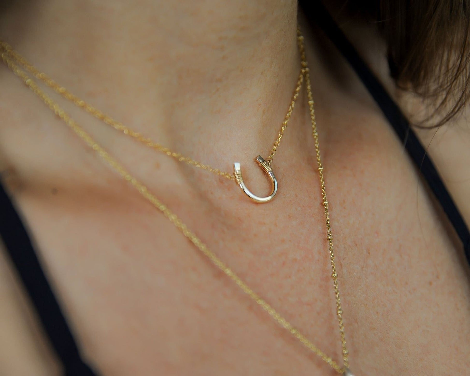 A close-up view of a woman's neck adorned with a delicate gold necklace featuring a small horseshoe pendant.