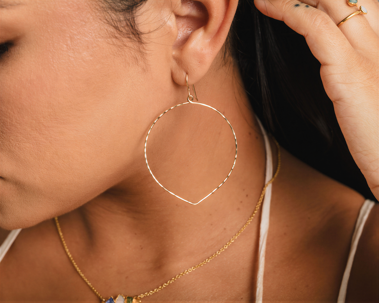 A close-up view of a woman's face, focusing on her large hoop earrings and necklace.
