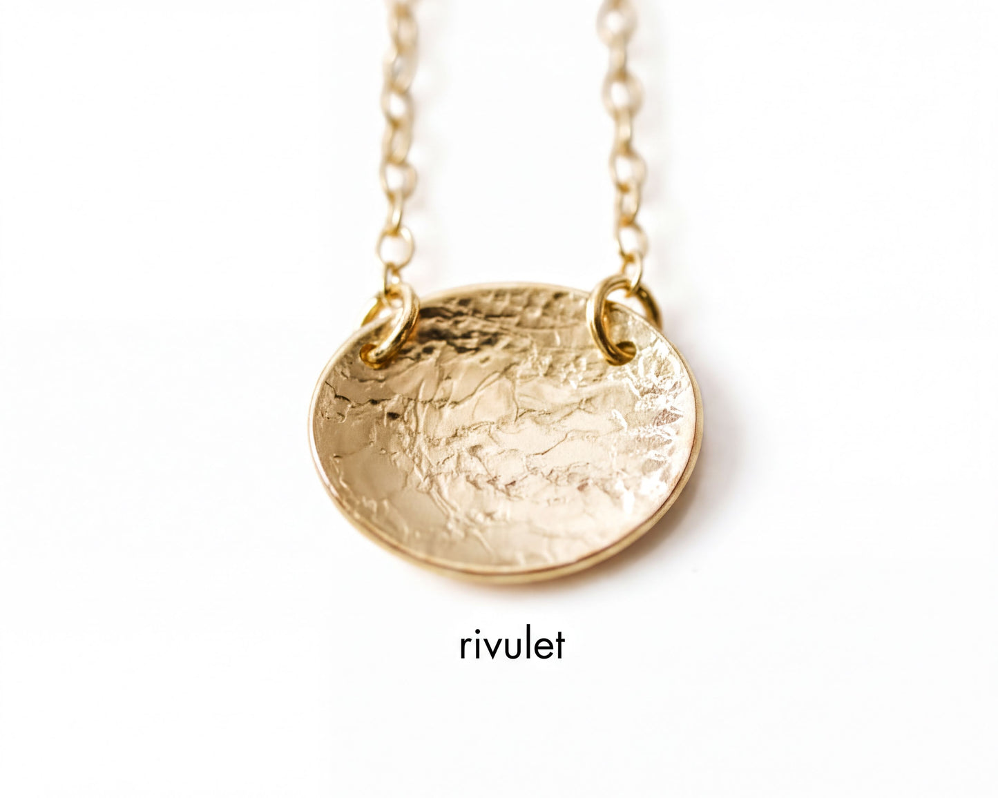 A close-up image of a gold-colored necklace with a textured oval pendant.