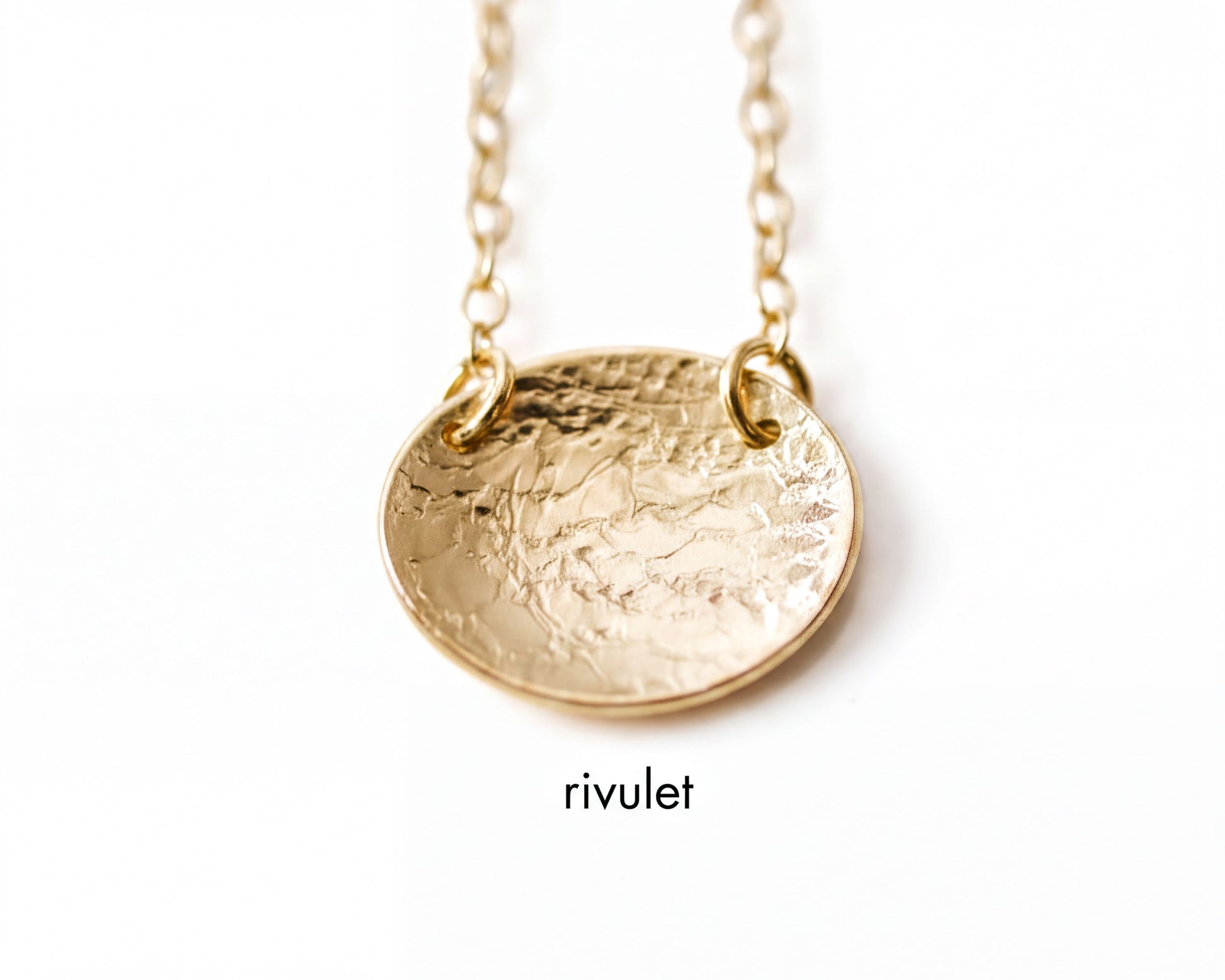 A close-up image of a gold-colored necklace with a textured oval pendant.