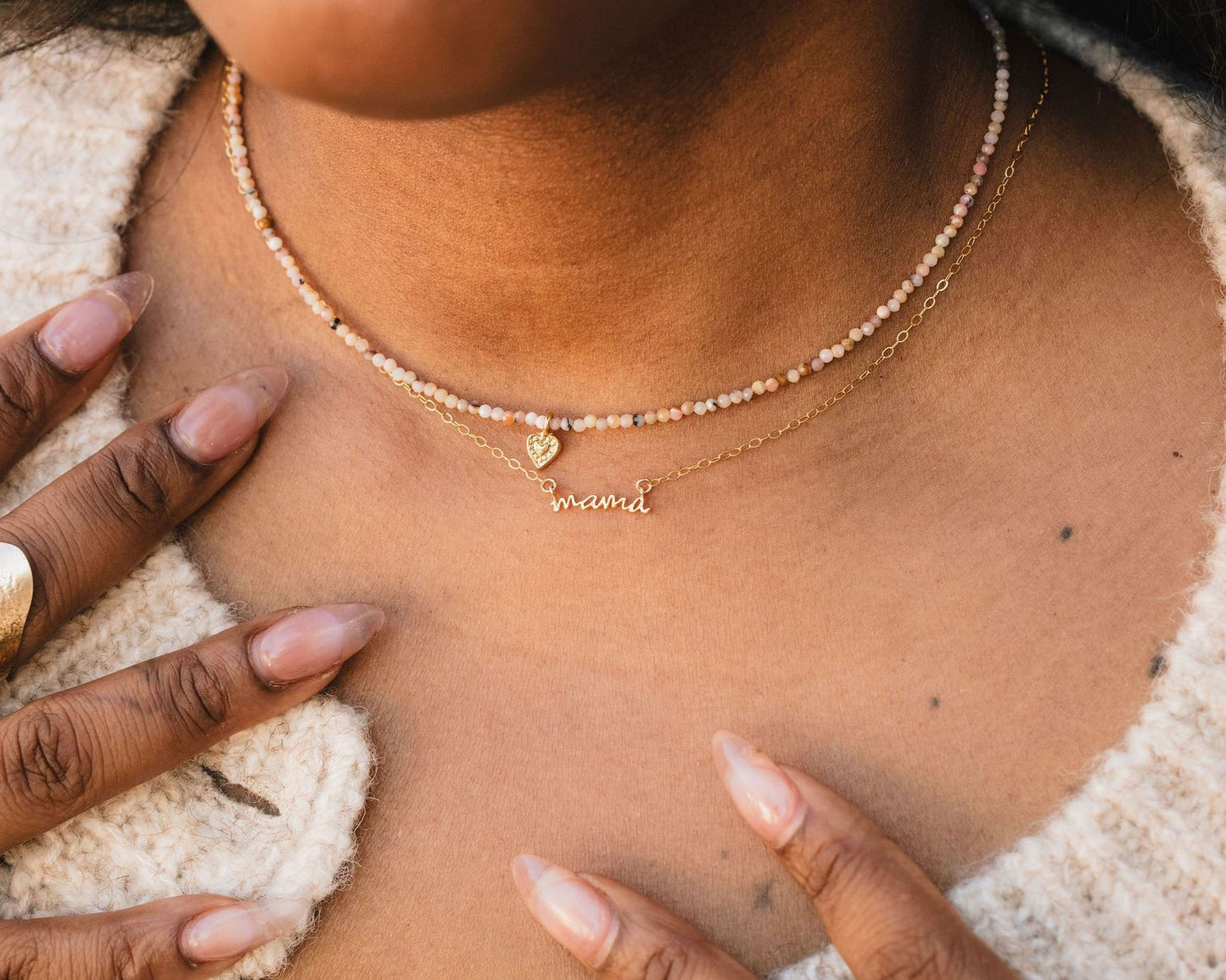 A close-up of a person's neck and chest area, featuring a necklace with a pendant and a small charm.