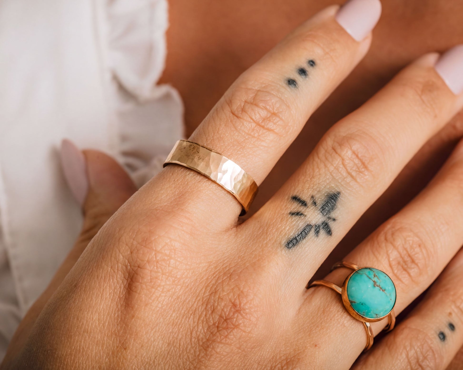 A close-up of a person's hand wearing three rings on different fingers, with a tattoo visible on one of the fingers.