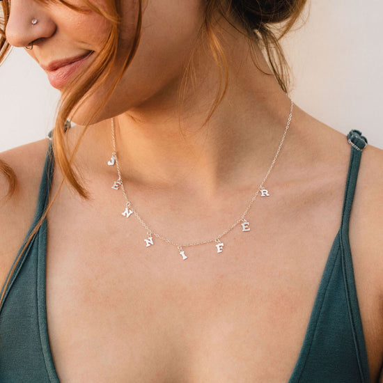 A woman wearing a necklace with the name "JENNY" engraved on it.
