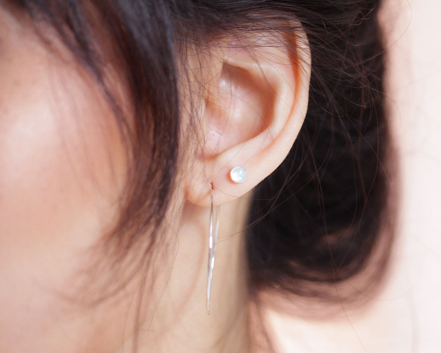 A close-up view of a person's ear with a pair of silver earrings featuring a round stone or gemstone.