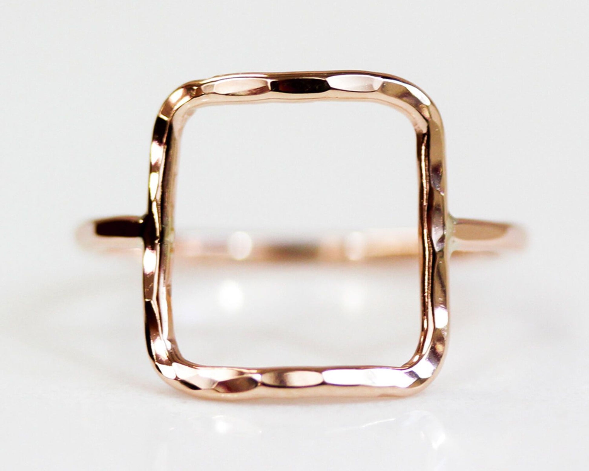 A simple, square-shaped gold ring with a textured, hand-forged design.