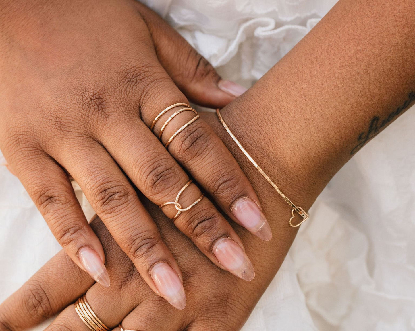 A close-up image of a person's hands wearing multiple rings and a bracelet.