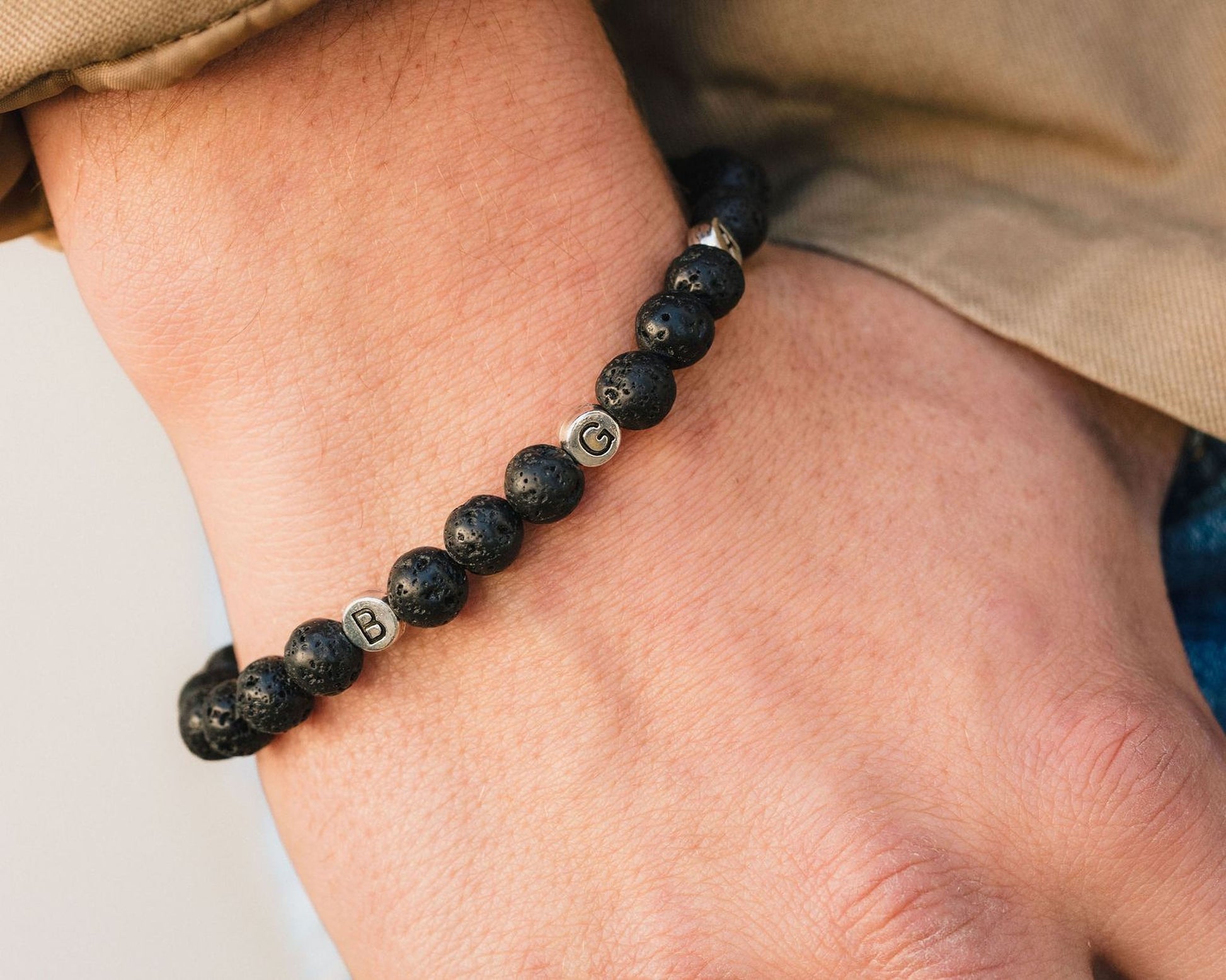 A close-up of a person's wrist wearing a bracelet made of black beads with letters on them.