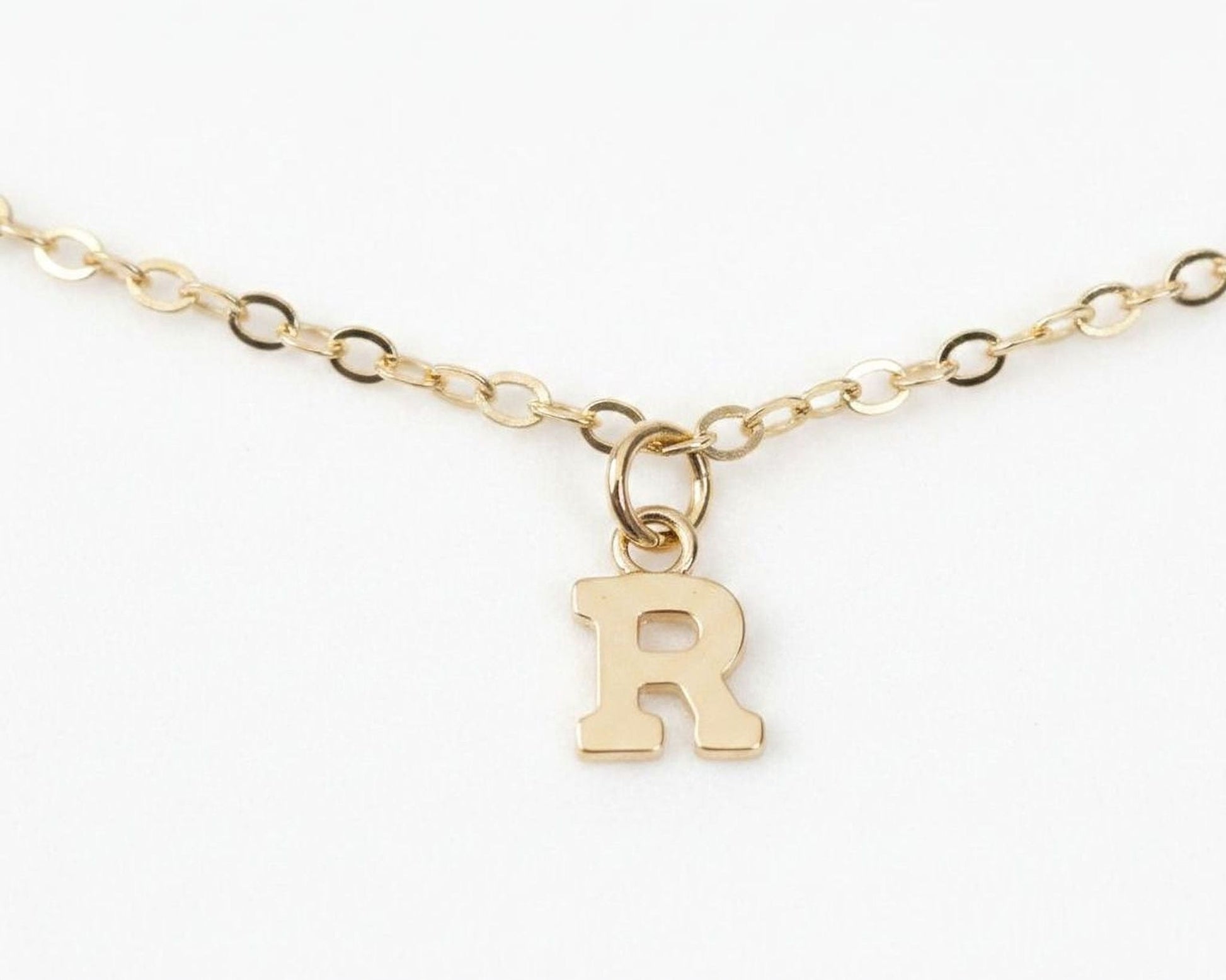 A gold-colored initial charm with a small loop at the top, attached to a chain.
