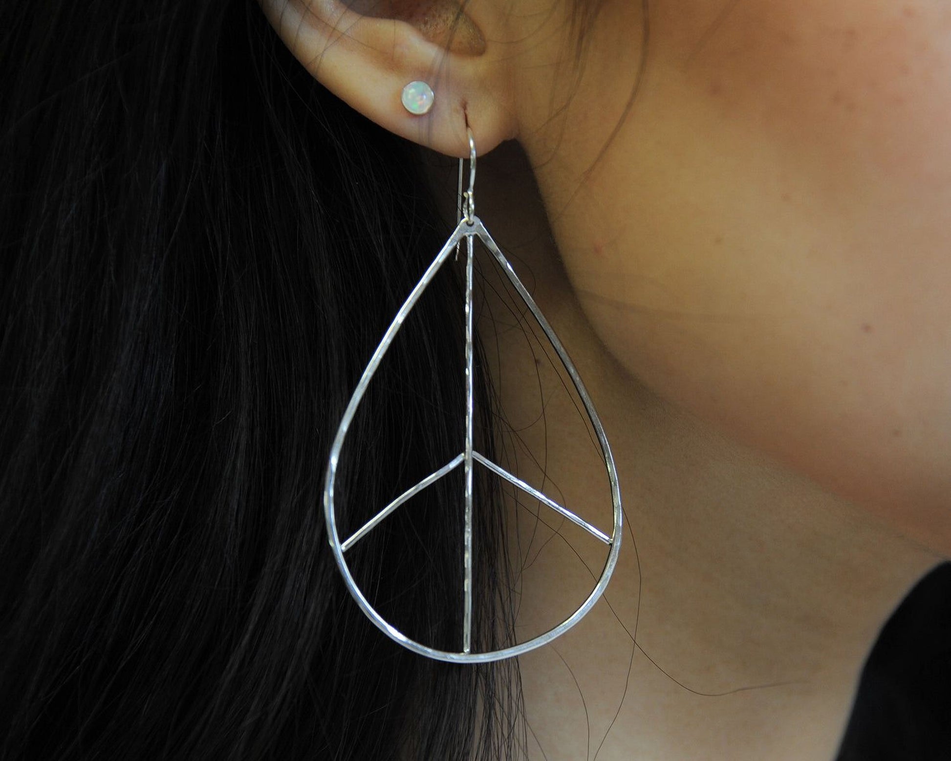 A close-up view of a person's ear wearing a pair of silver earrings with a peace sign design.