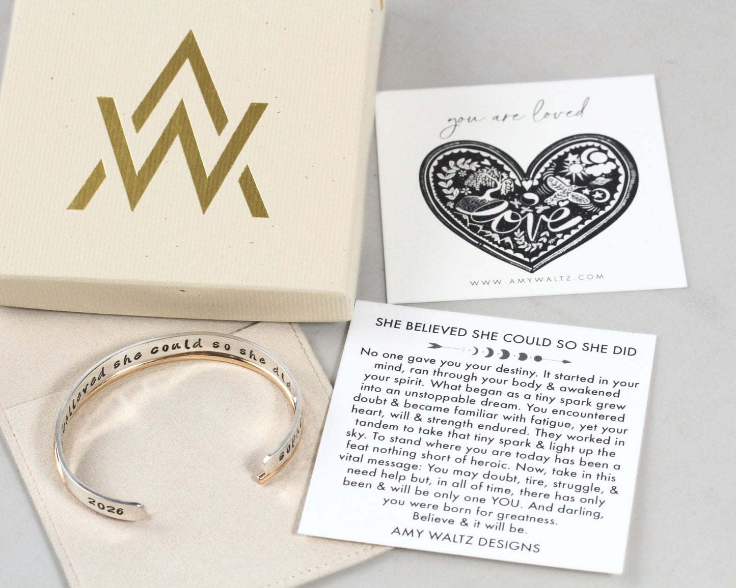 a bracelet, a card with a heart-shaped design, and a box with a gold and black logo.