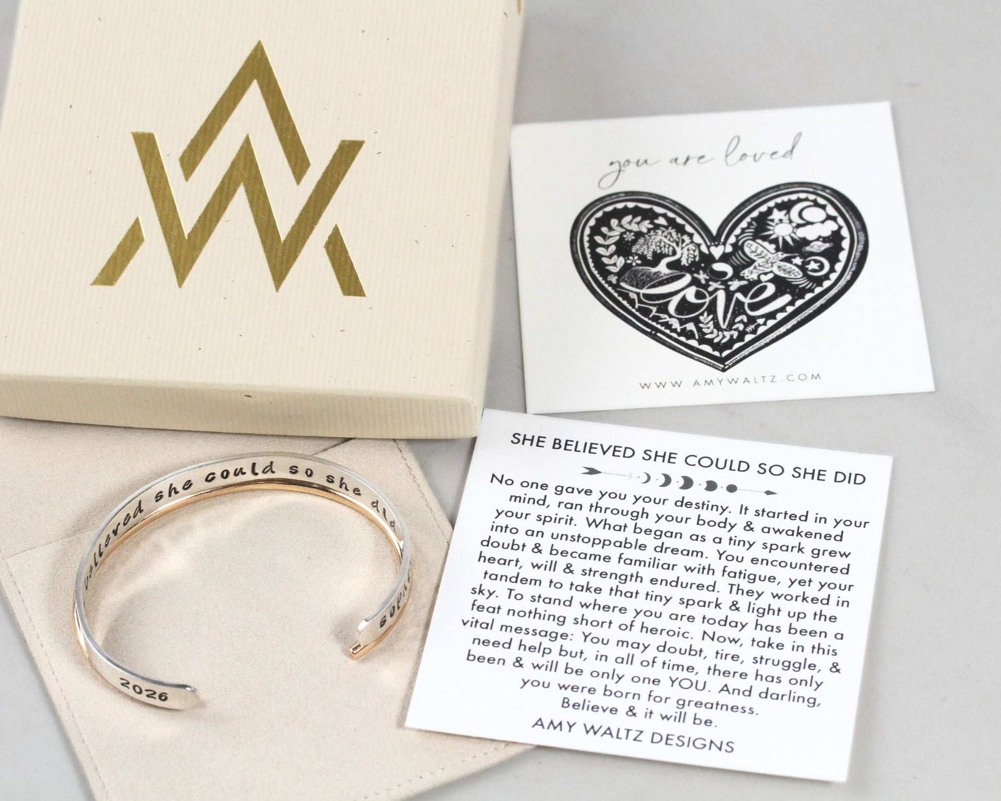 a bracelet, a card with a heart-shaped design, and a box with a gold and black logo.