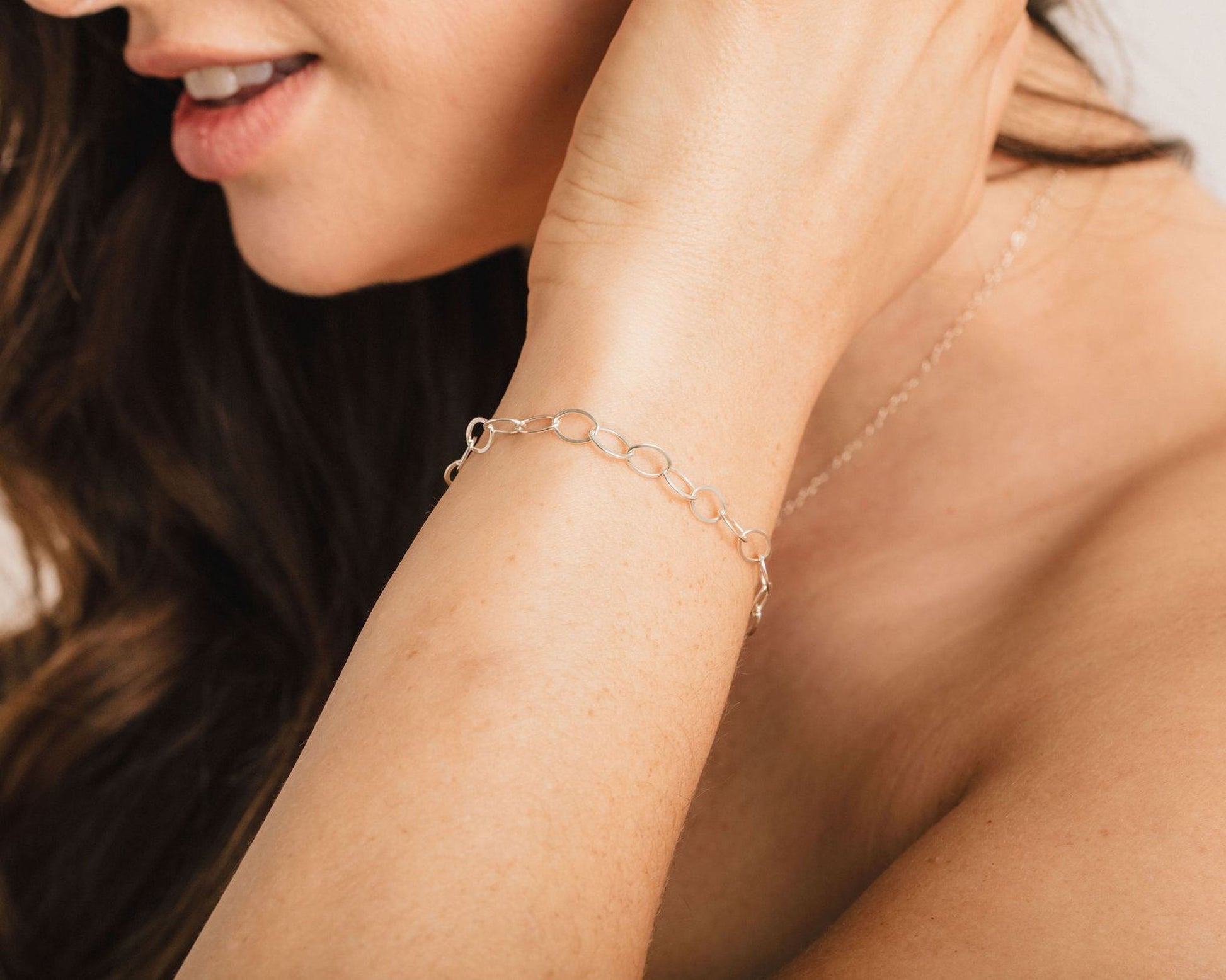 A close-up of a woman's arm wearing a silver bracelet, with her hair visible in the background.