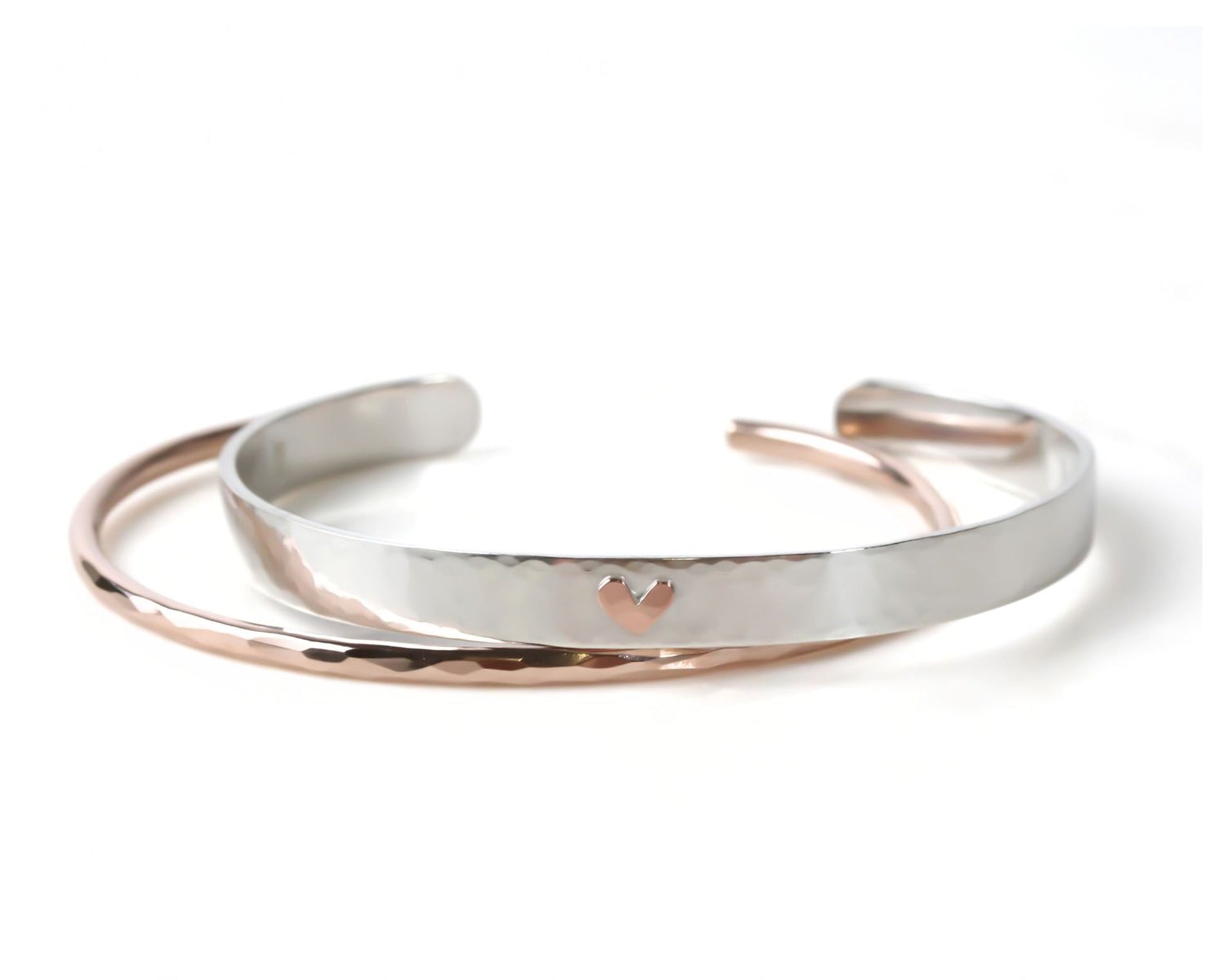 A pair of silver and gold cuff bracelets with a heart-shaped charm on the center.