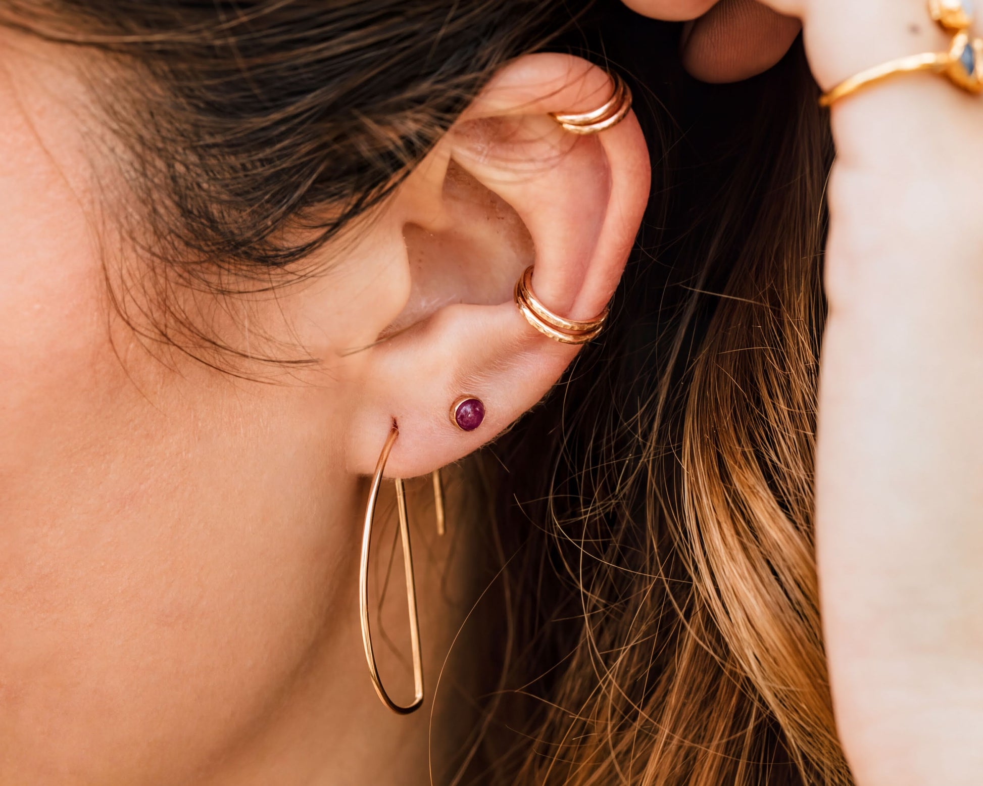 A close-up view of a person's ear adorned with multiple gold hoop earrings and a small gemstone earring.