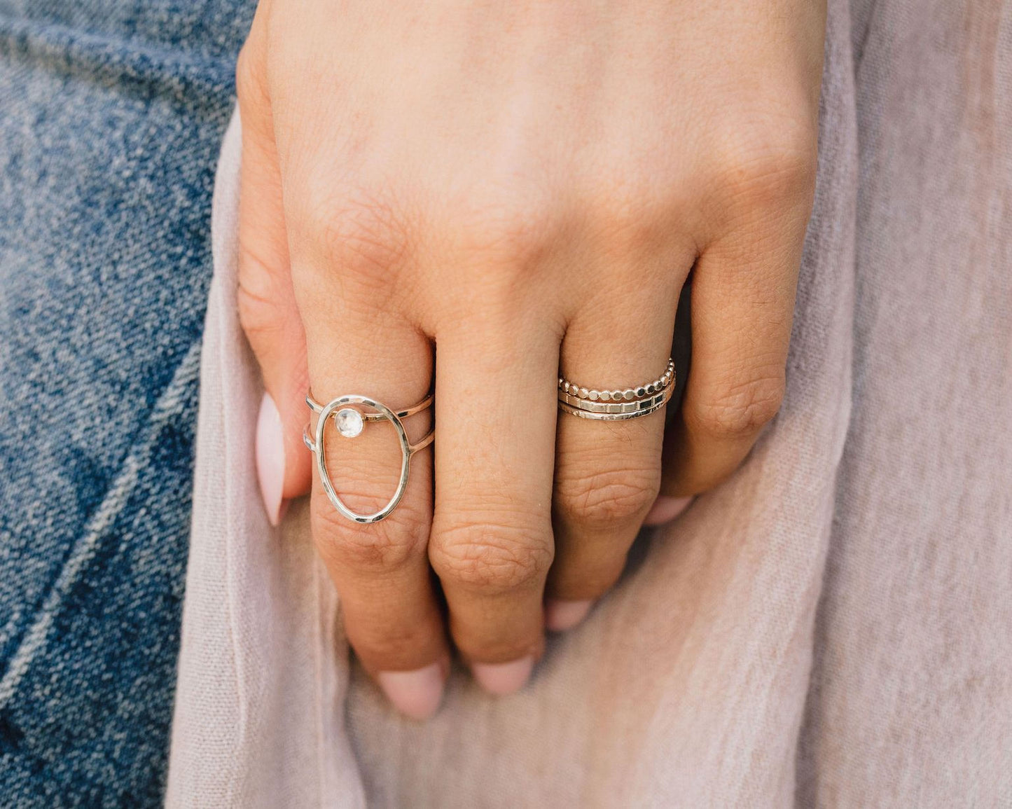 A close-up view of a person's hand wearing multiple rings, including a ring with a small stone or gemstone in the center.