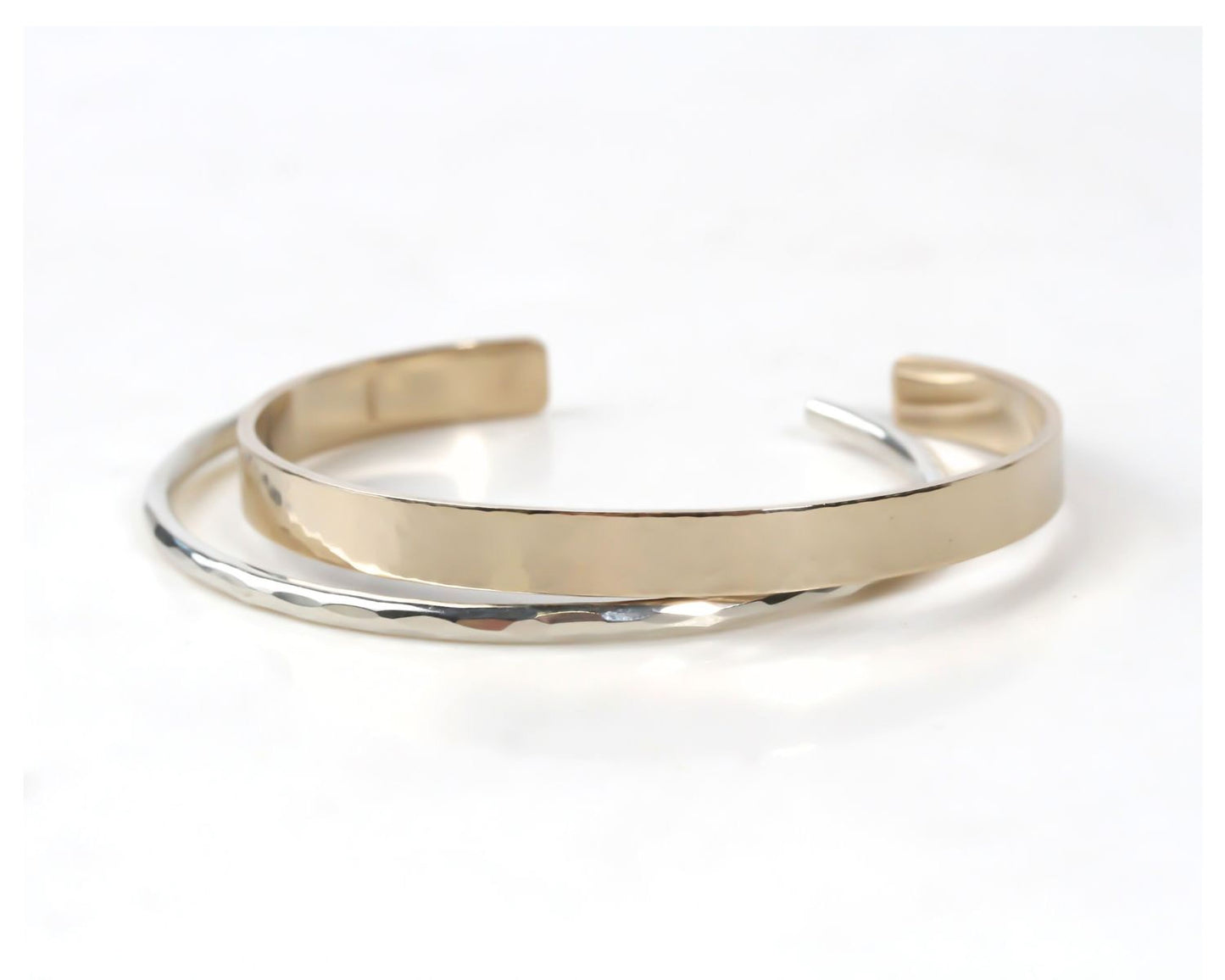 A gold and silver bracelet with a textured surface, resting on a white background.