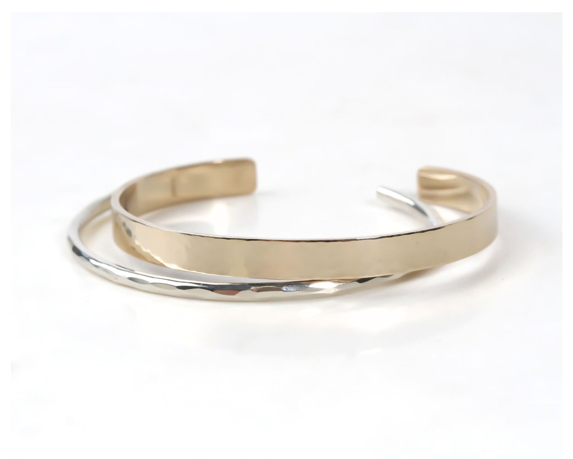 A gold and silver bracelet with a textured surface, resting on a white background.