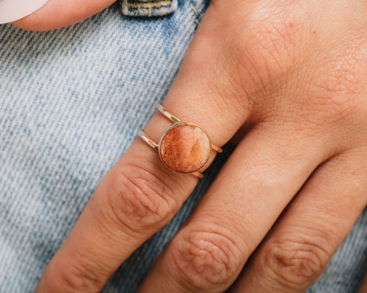 A close-up view of a person's hand wearing a ring with a large, round stone in the center.