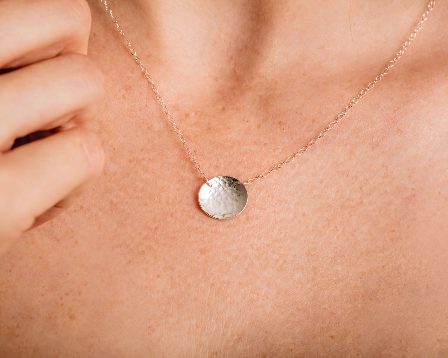 A close-up view of a person's neck and chest area, featuring a delicate silver necklace with a round pendant.