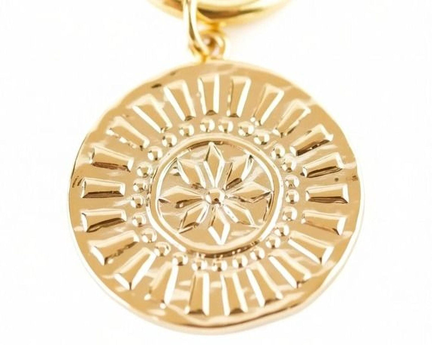 A close-up image of a gold-colored pendant with a detailed design featuring a sun-like motif.