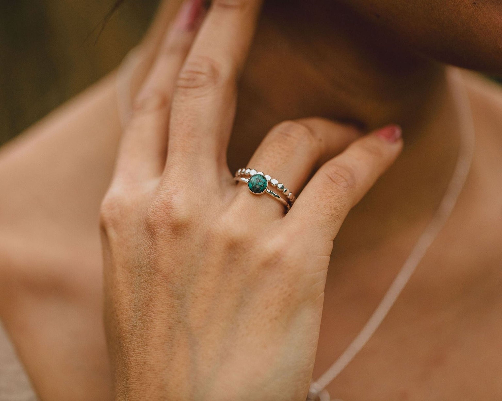 A close-up of a person's hand wearing a ring with a green gemstone.