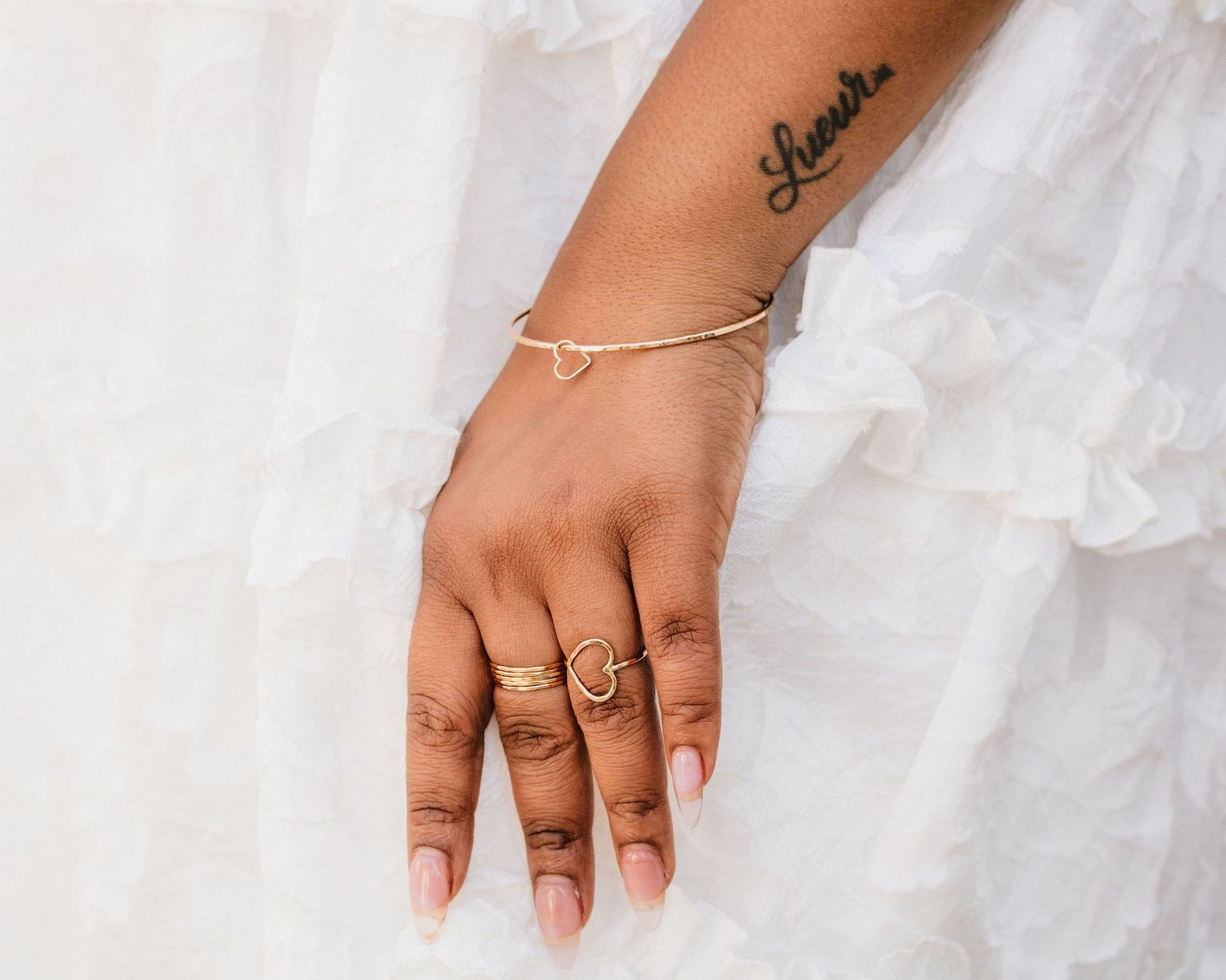 A close-up of a person's hand wearing multiple rings and a bracelet, with a tattoo visible on the wrist.