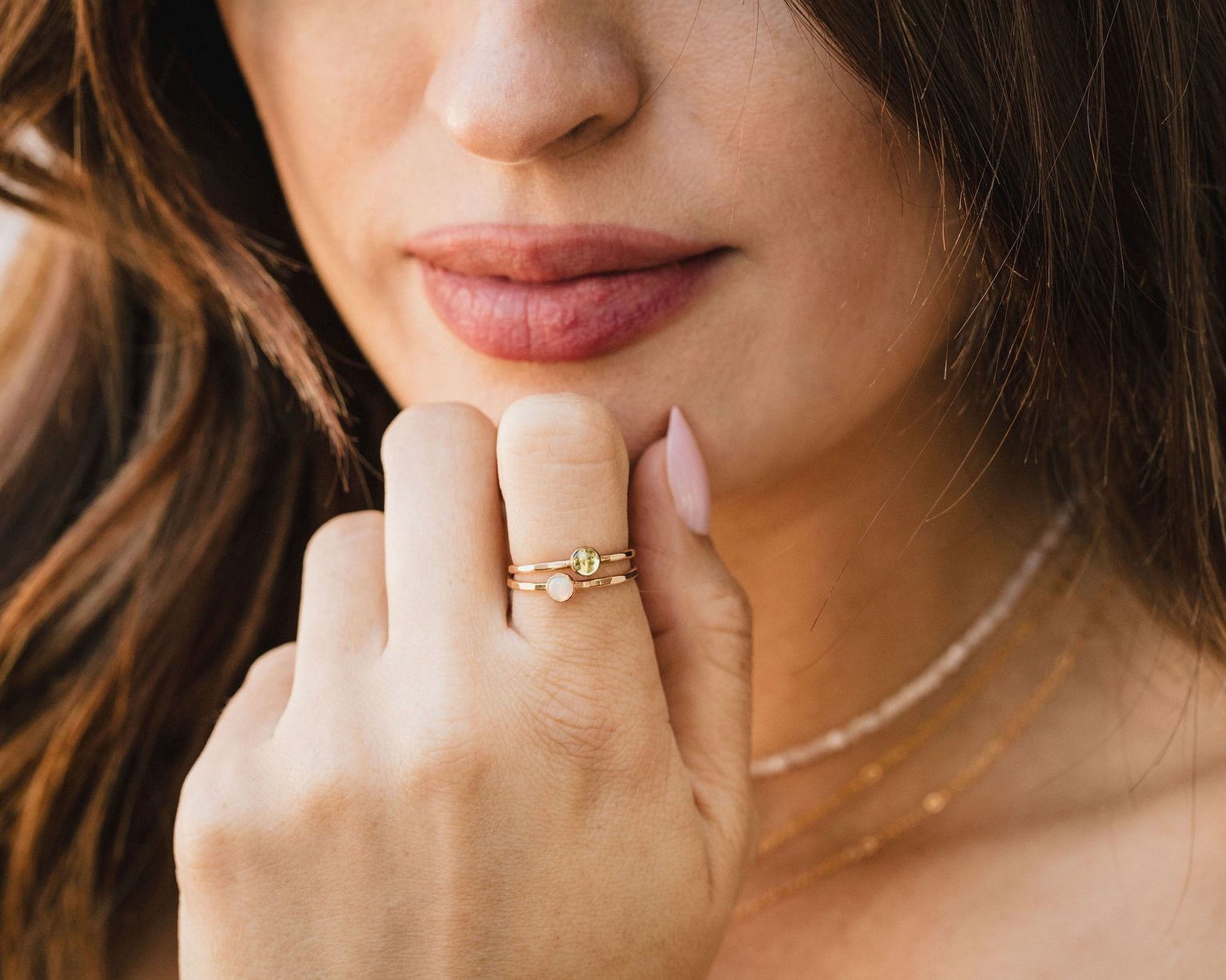A close-up of a woman's face, focusing on her hand and fingers adorned with a ring and a necklace.