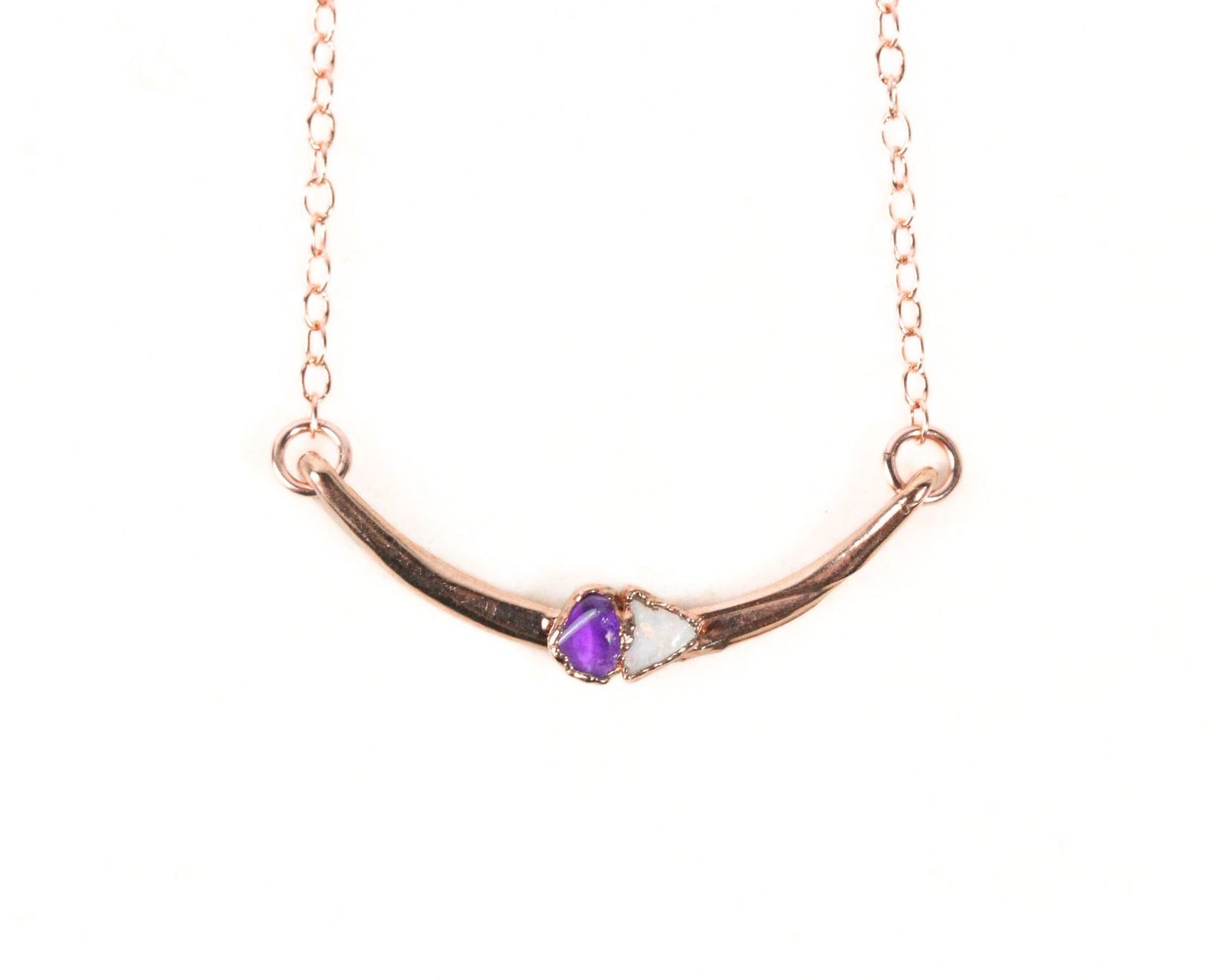 A necklace with a curved metal bar and a purple gemstone in the center.