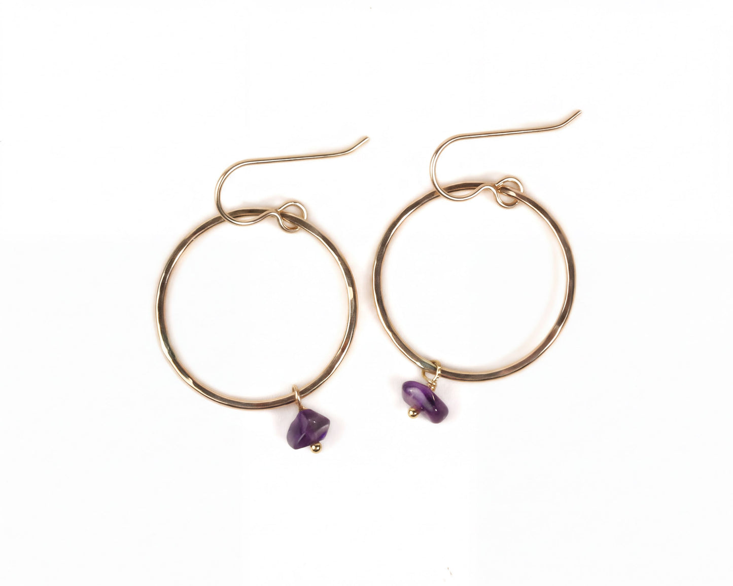 A pair of gold hoop earrings with purple gemstones hanging from them.