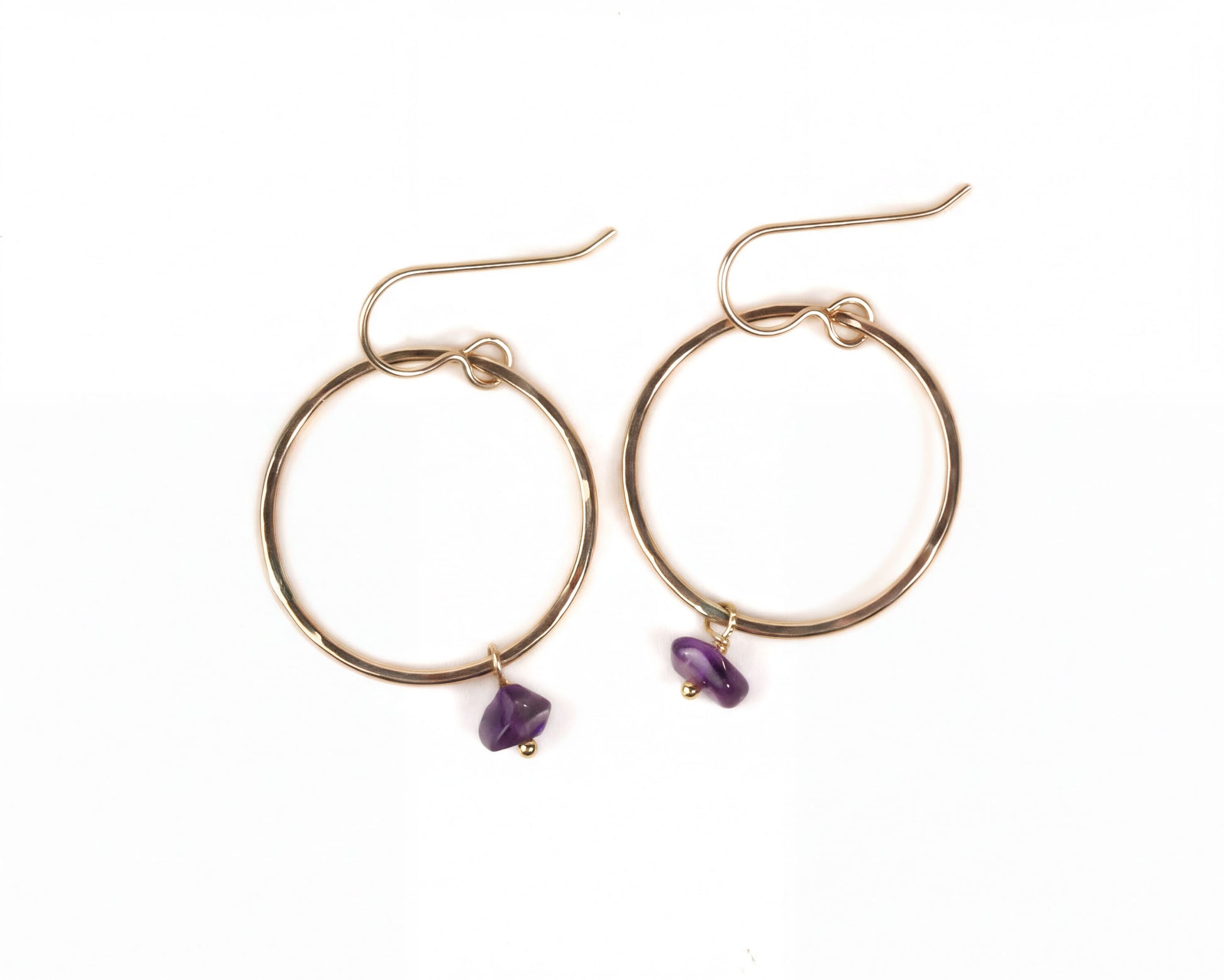 A pair of gold hoop earrings with purple gemstones hanging from them.