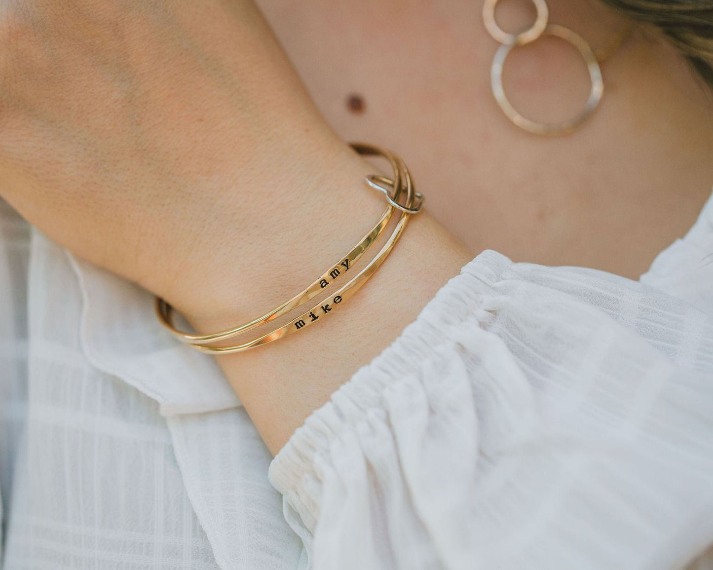 A close-up view of a person's wrist wearing a gold-colored bracelet with the word "MAKE" engraved on it.