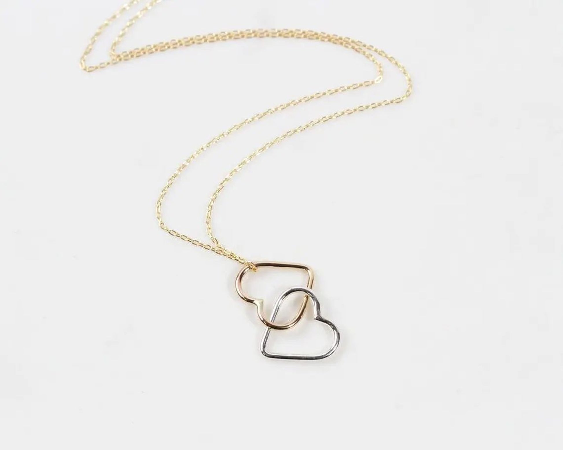 A delicate gold necklace with a heart-shaped pendant in silver and gold tones.