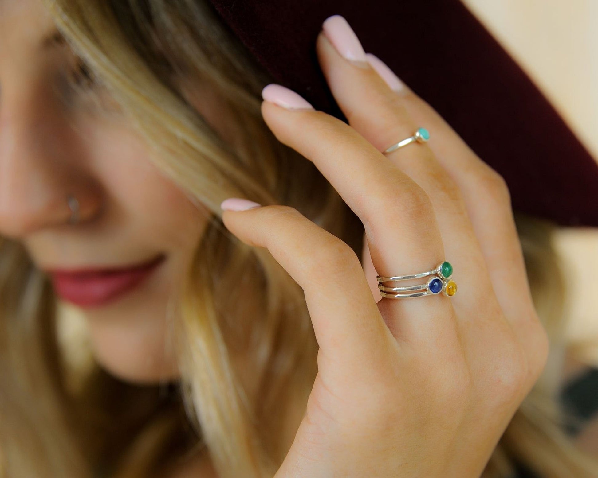 A close-up of a person's hand wearing three rings on different fingers, with a maroon hat partially visible in the background.