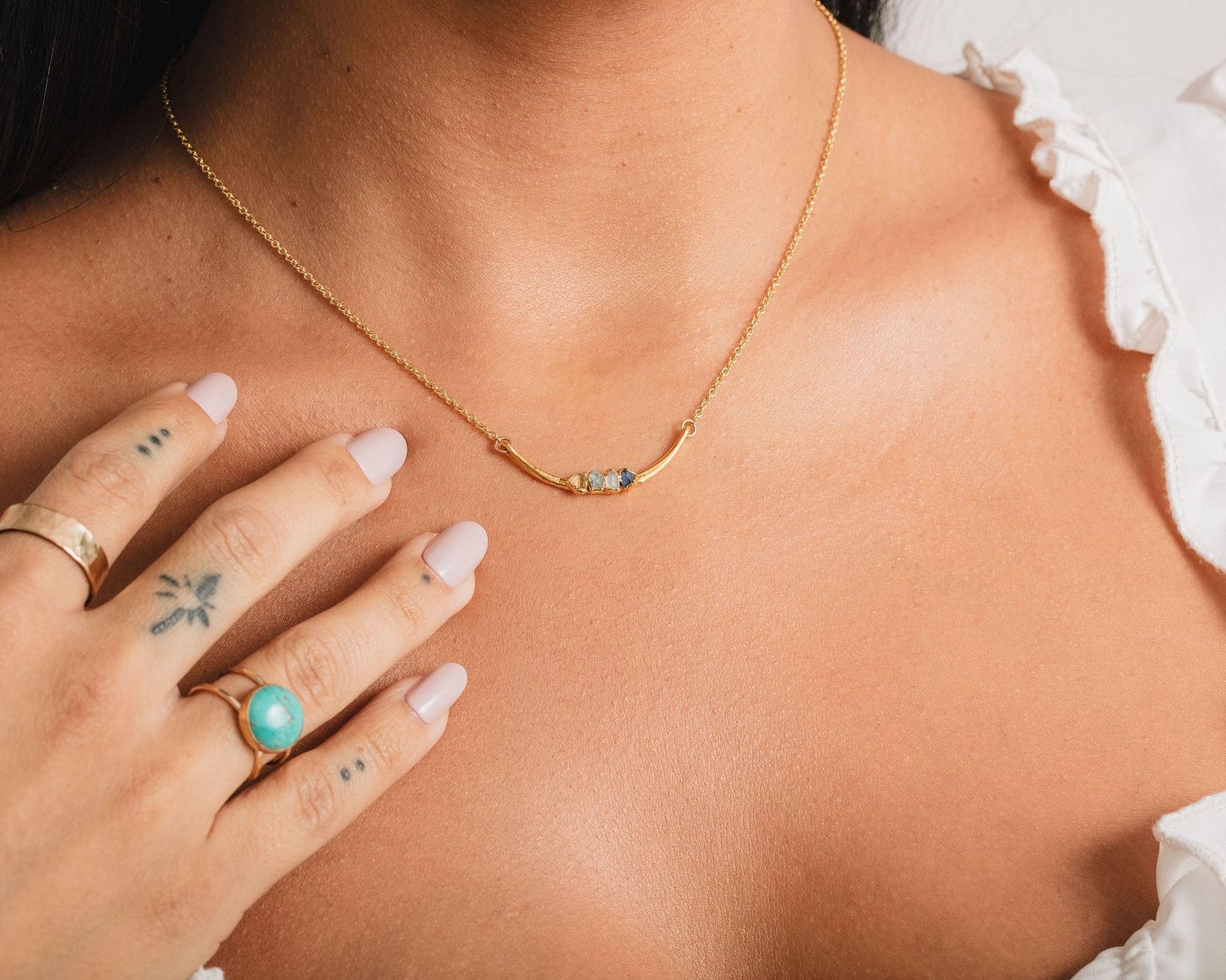 A close-up of a person's hand wearing a gold necklace and ring, with tattoos visible on the fingers.