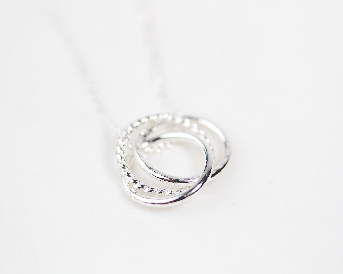 A silver necklace with a pendant in the shape of a twisted ring.