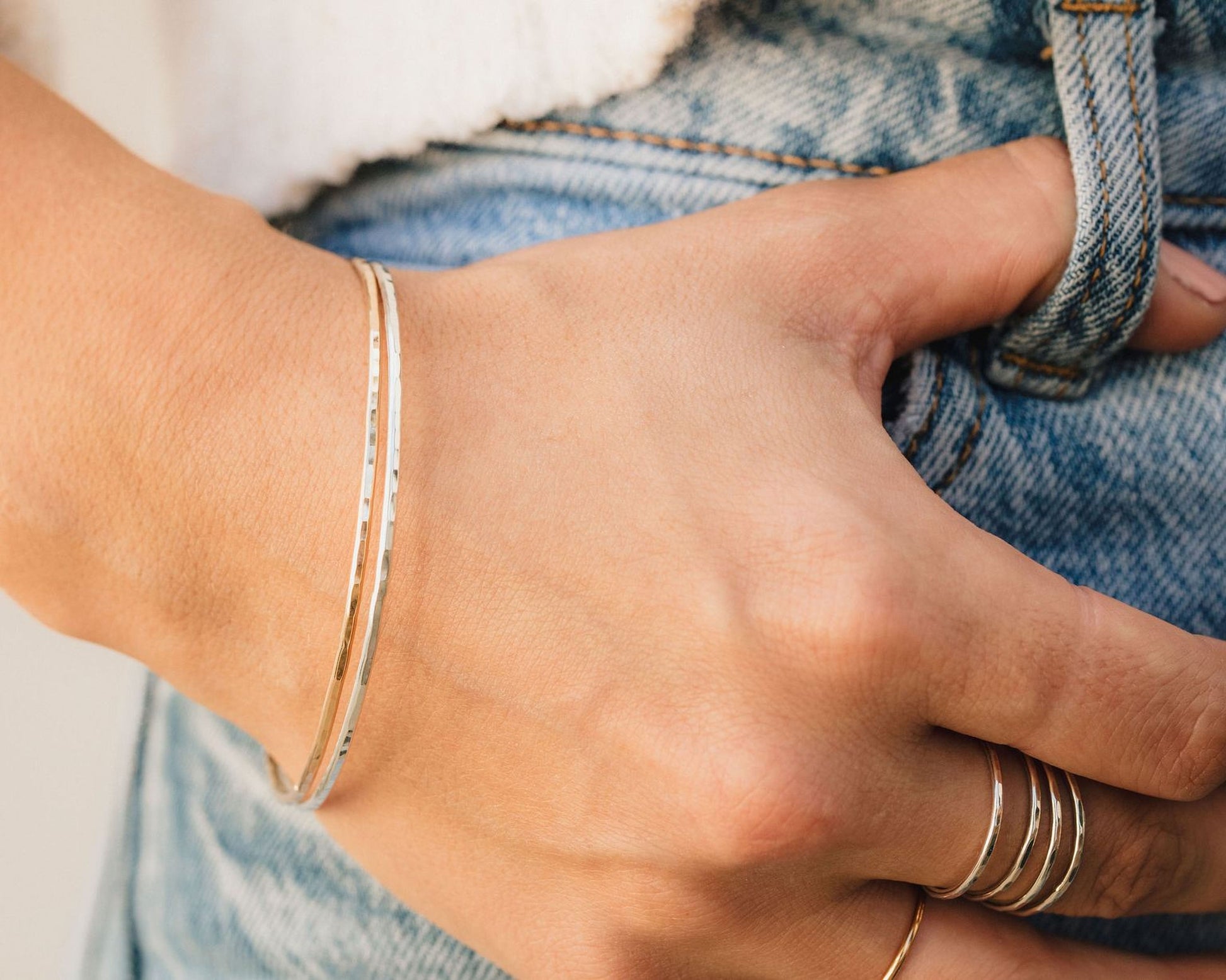A close-up view of a person's hand wearing a bracelet and rings on their fingers.
