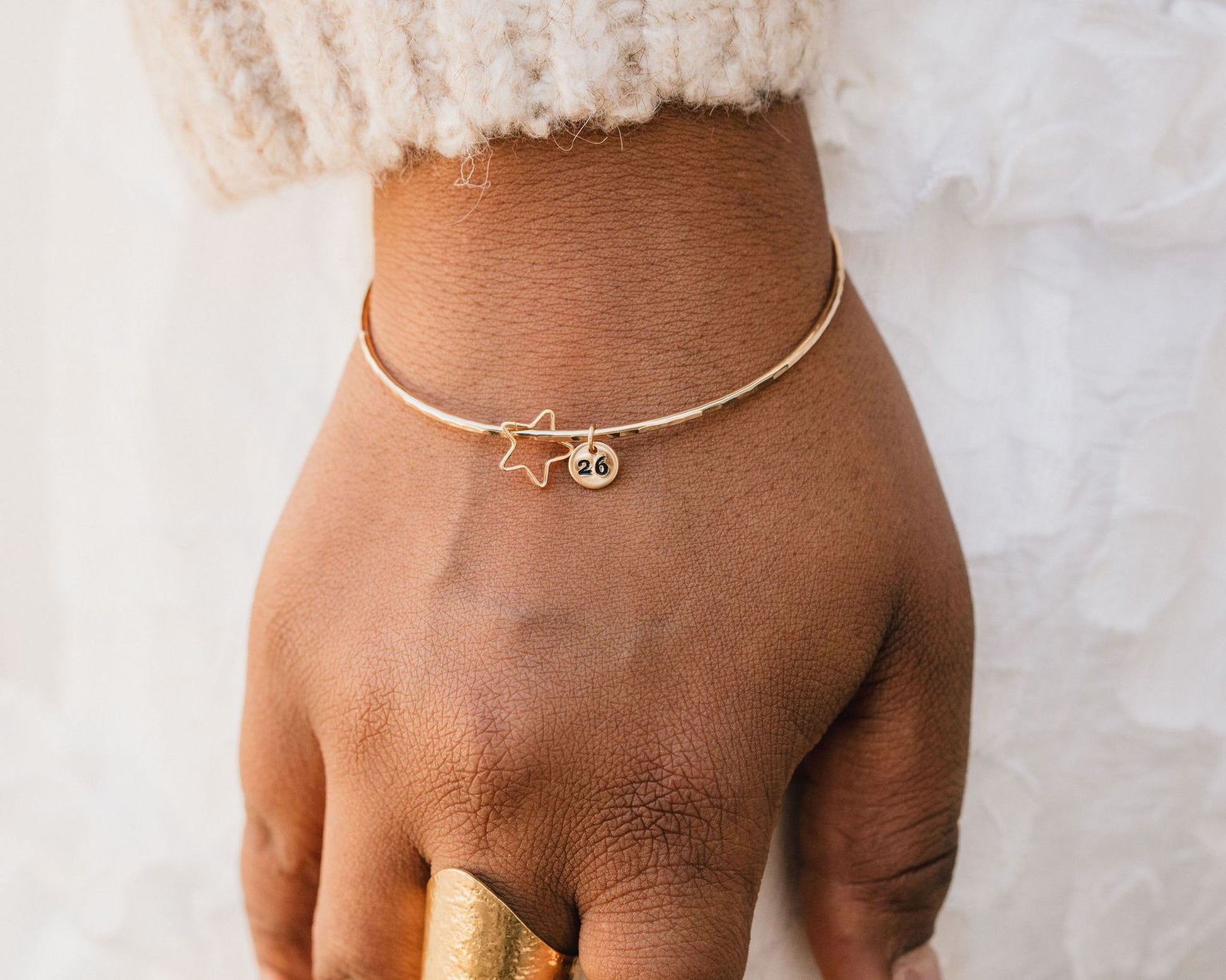 A close-up view of a person's hand wearing a gold bangle bracelet with a star charm and a small charm.