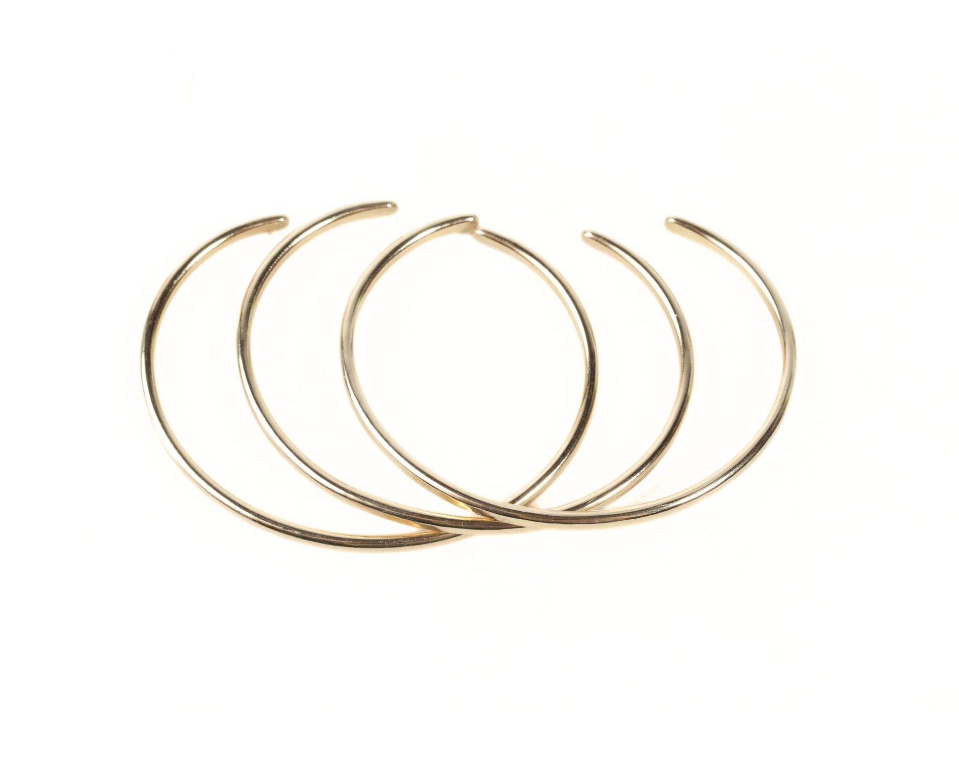 A group of gold-colored bracelets arranged in a circular pattern against a white background.