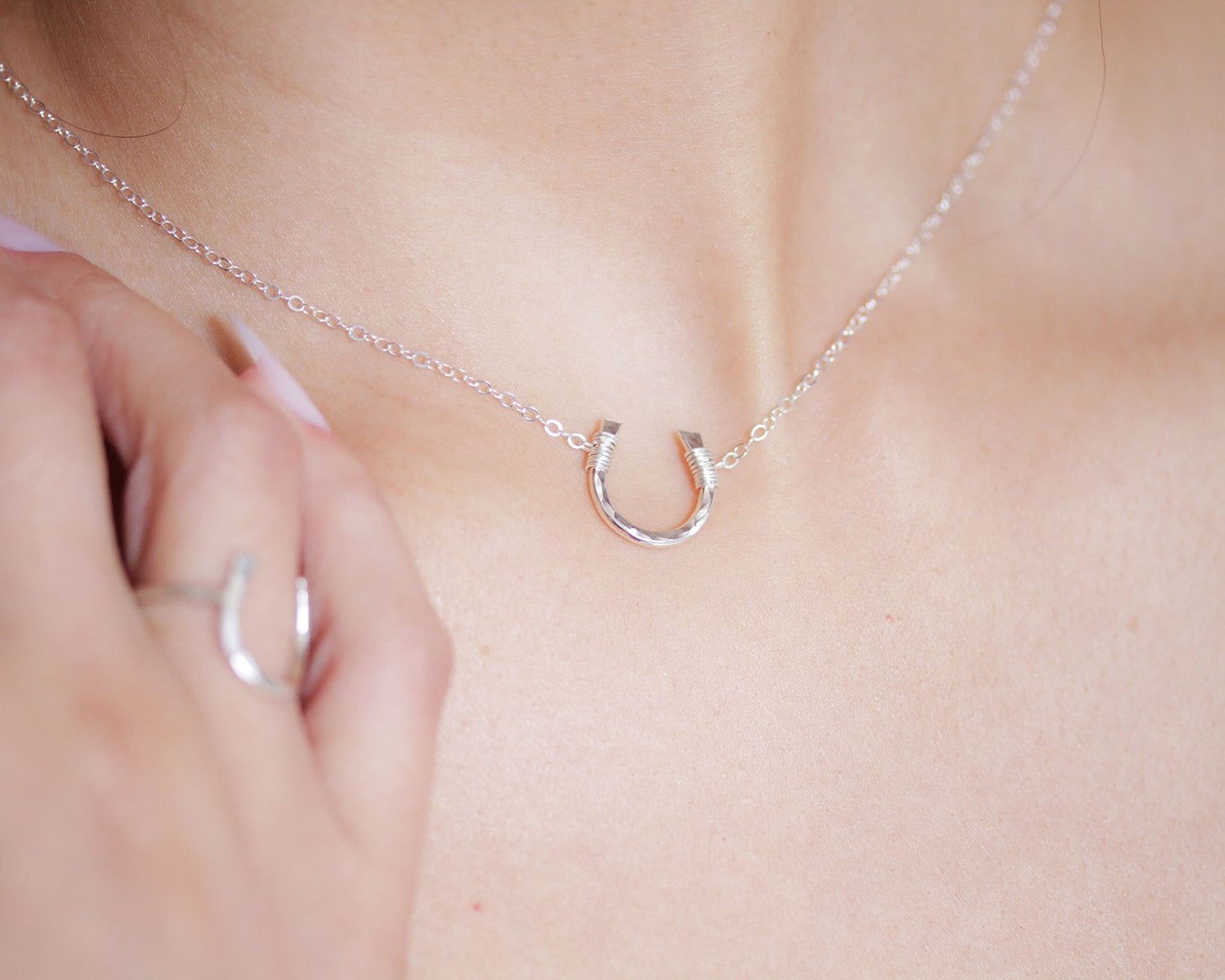A close-up view of a person's hand wearing a silver necklace with a horseshoe pendant.