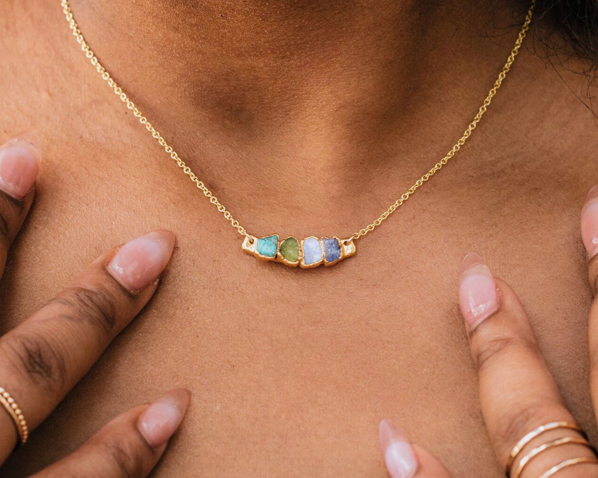 A close-up view of a gold necklace with a colorful gemstone pendant, worn around a person's neck.