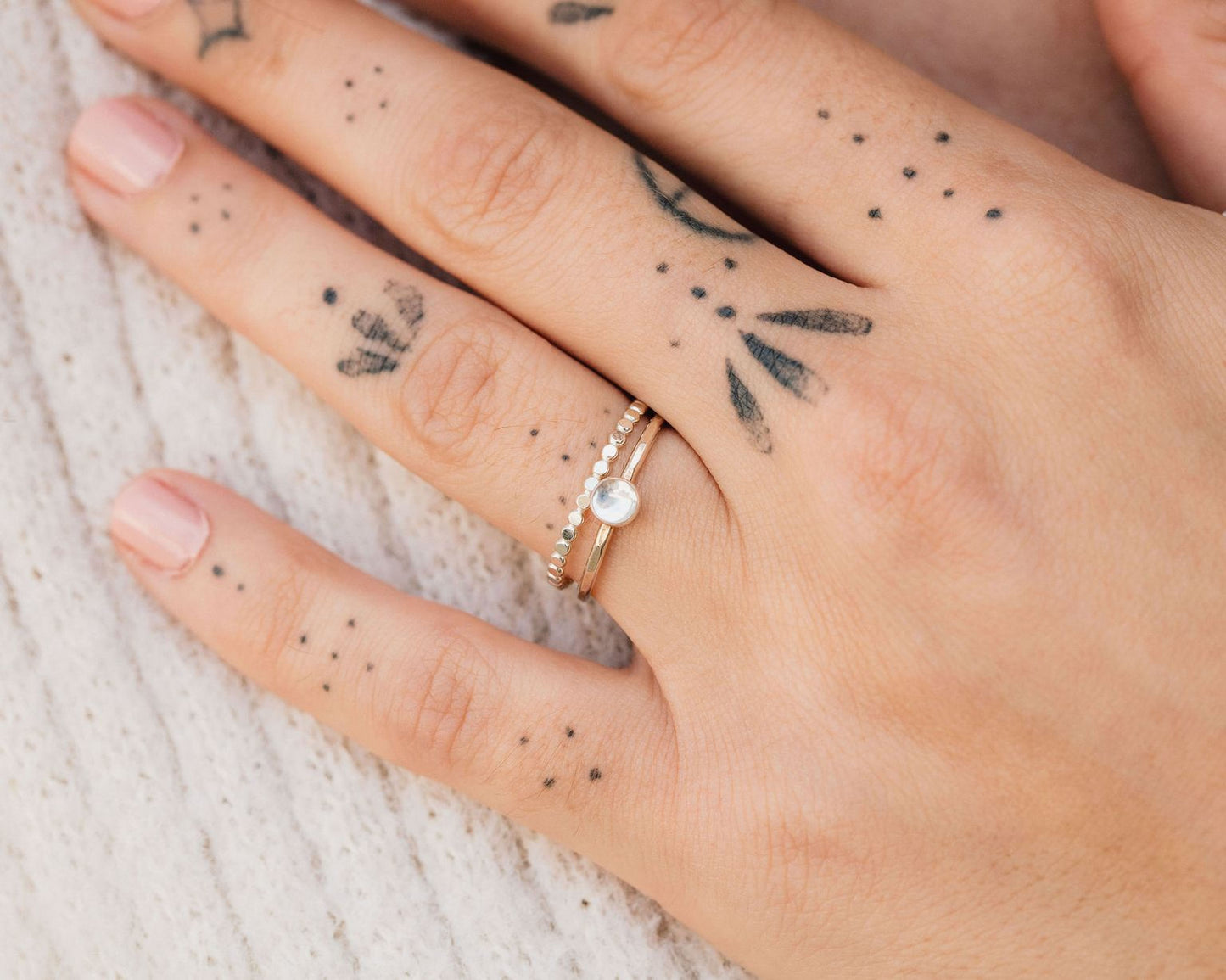 A close-up of a person's hand with a ring on one of the fingers and several tattoos on the fingers.