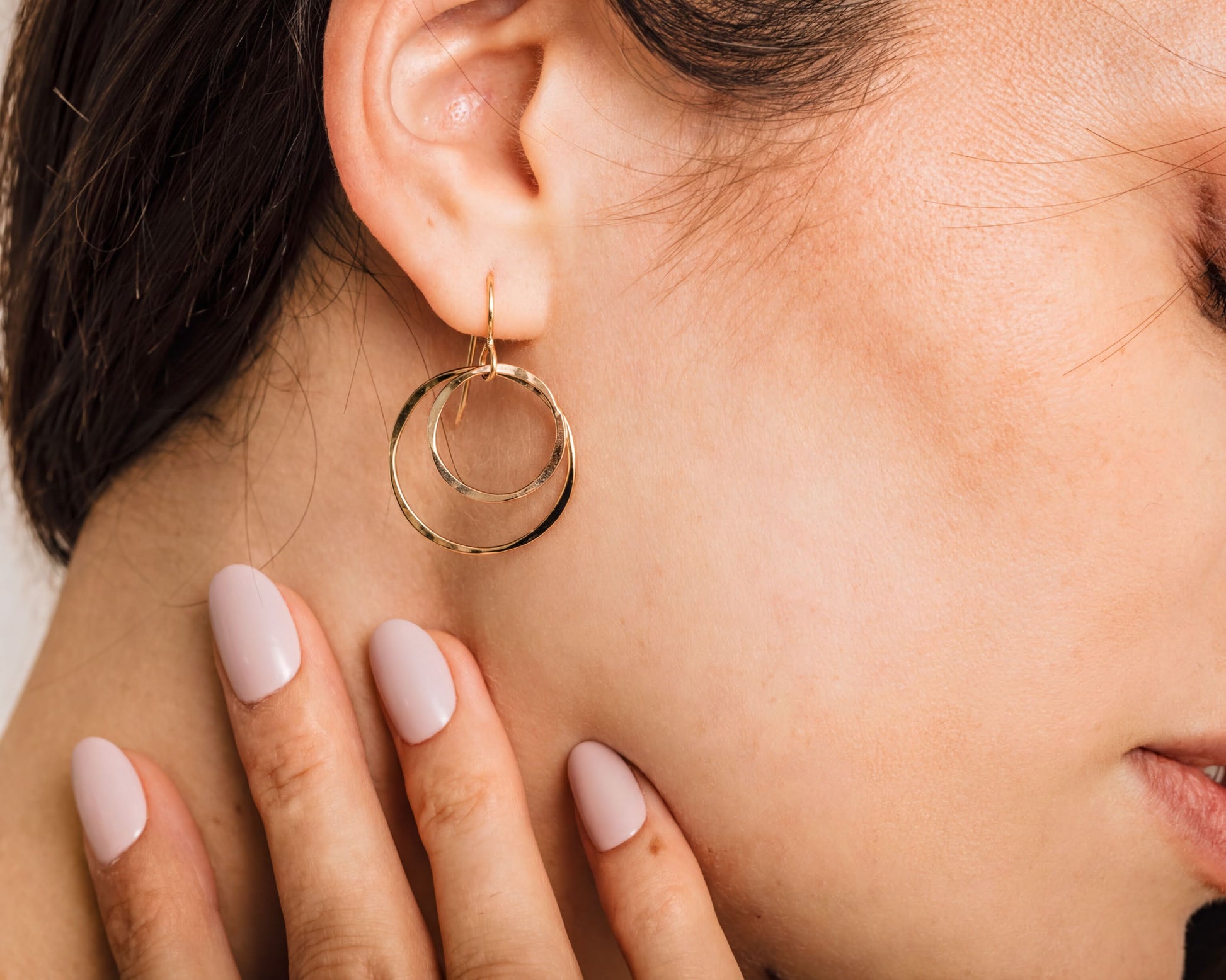 A close-up of a woman's face, focusing on her earrings and hand.