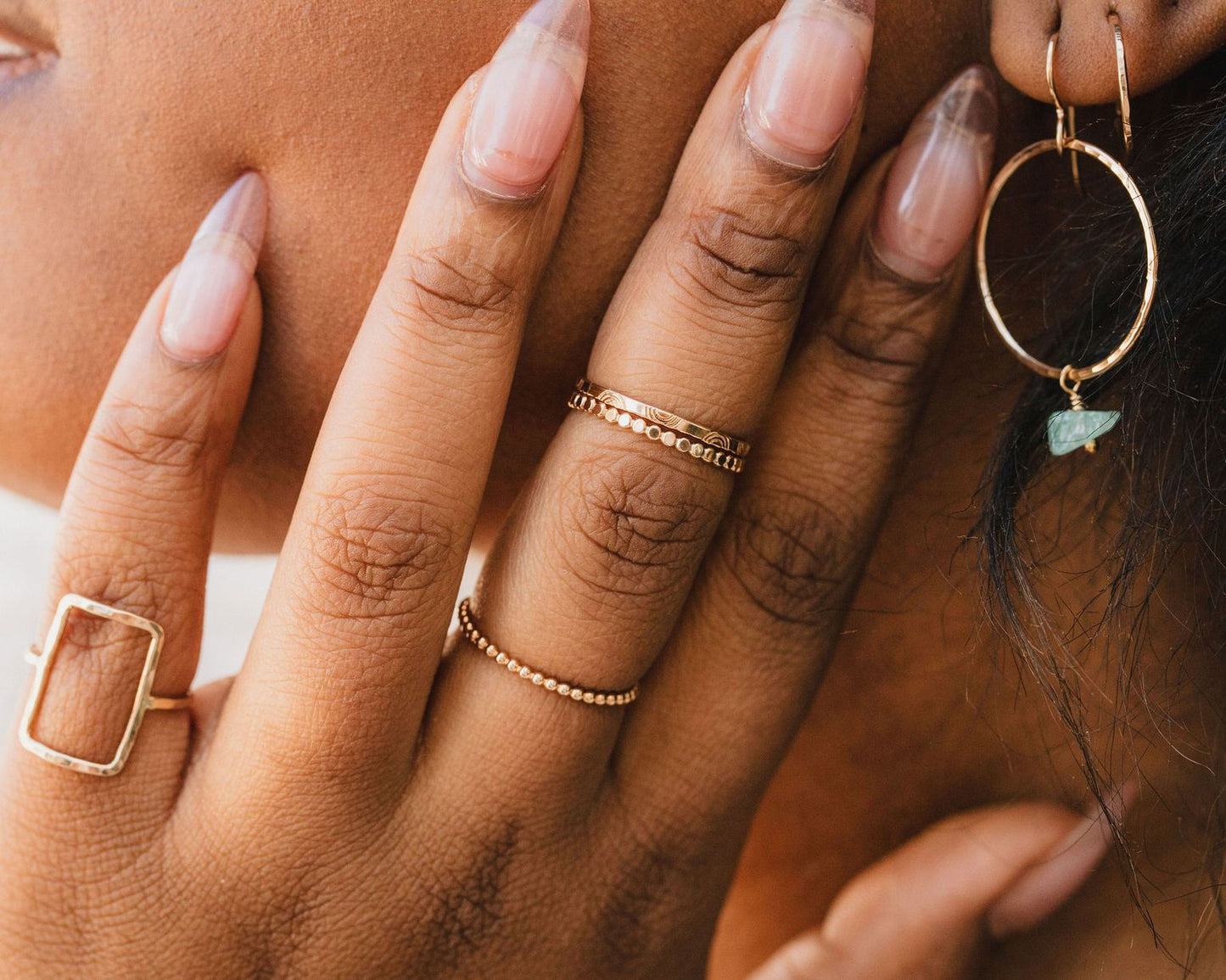 A close-up of a person's hand adorned with multiple rings and earrings, showcasing their fingers and the jewelry.