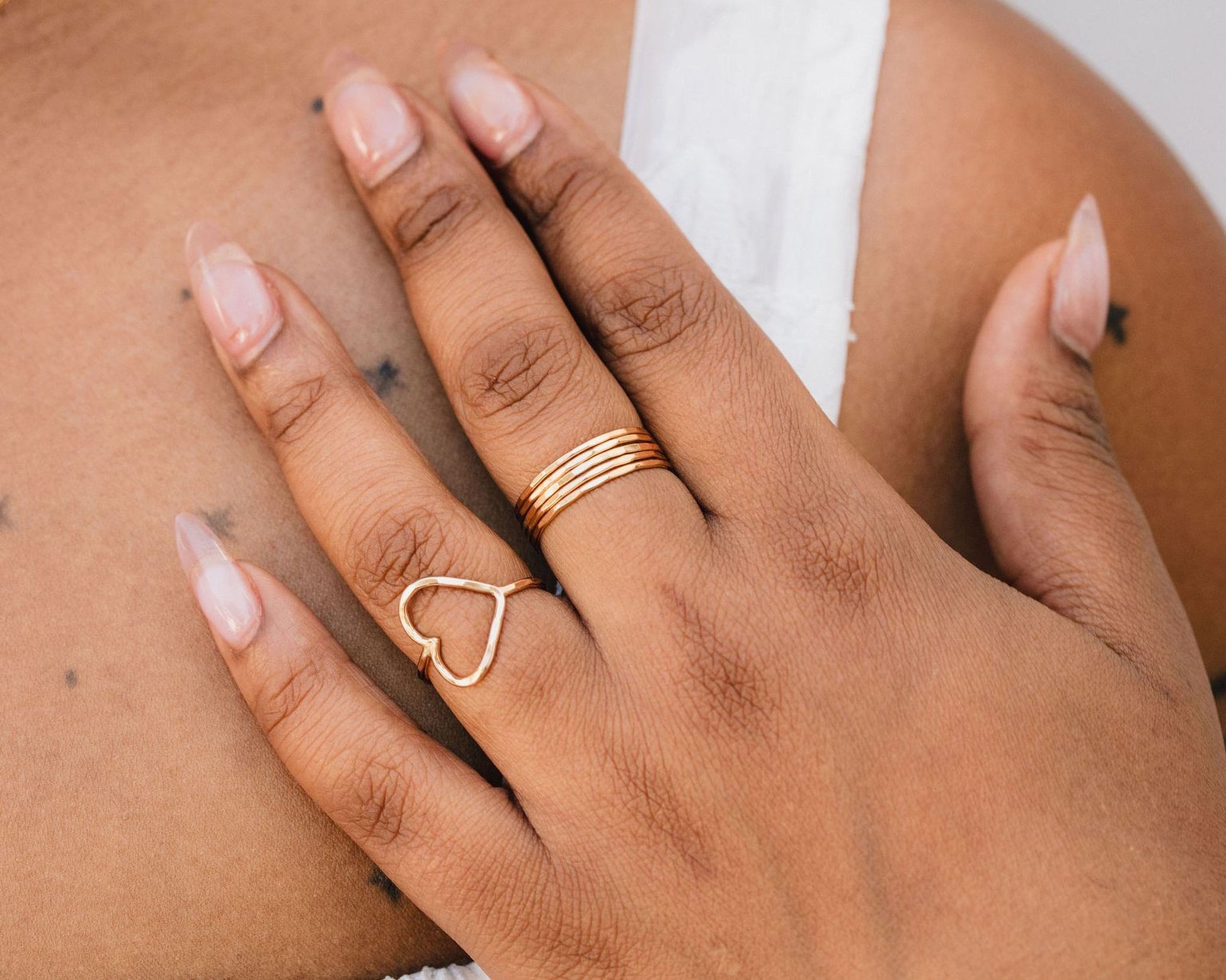 A close-up of a person's hand wearing multiple rings, including a heart-shaped ring and a ring with multiple tiers.