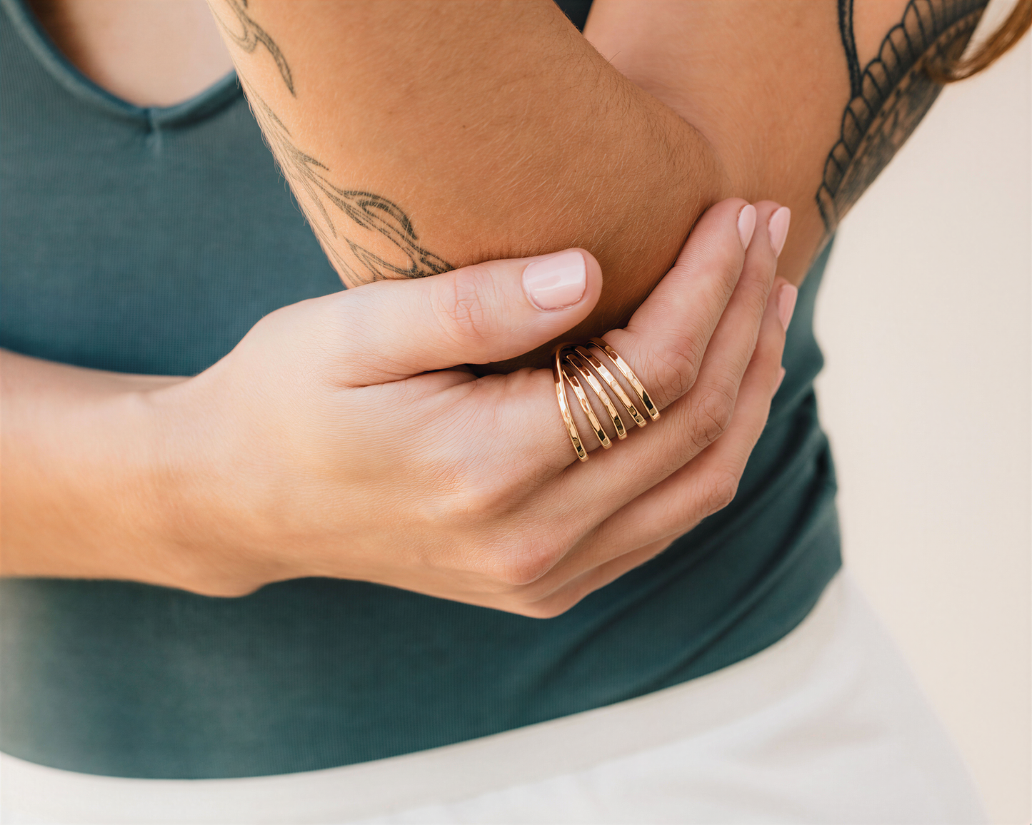 A close-up image of a person's hand wearing a ring and holding their arm with their other hand.