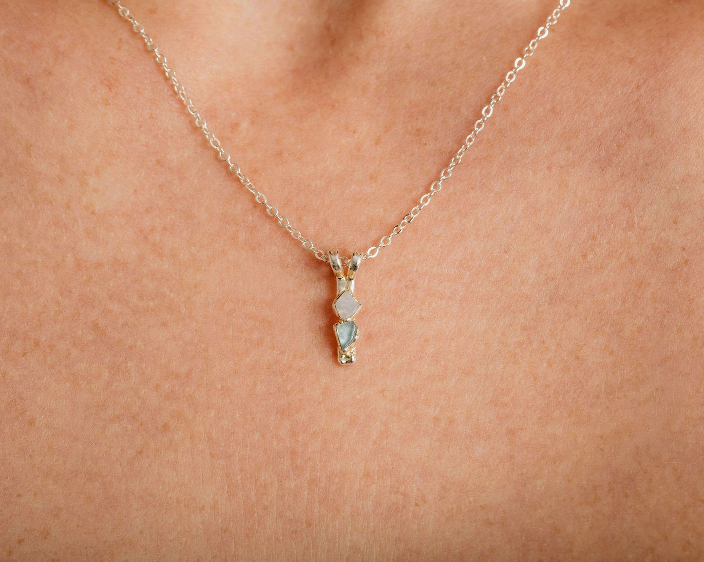 A close-up view of a delicate silver necklace with a small pendant featuring three small stones.