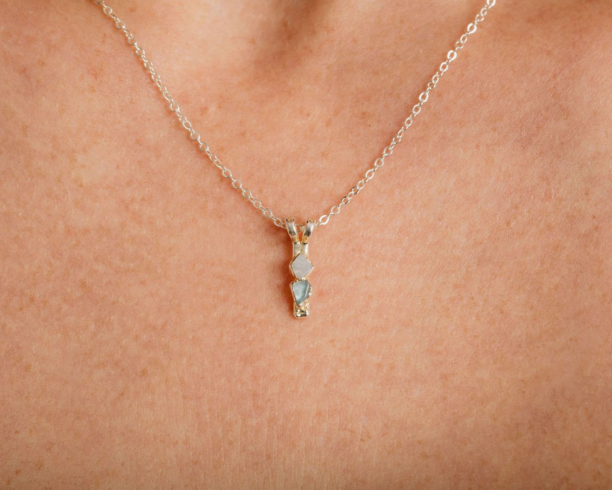A close-up view of a delicate silver necklace with a small pendant featuring three small stones.