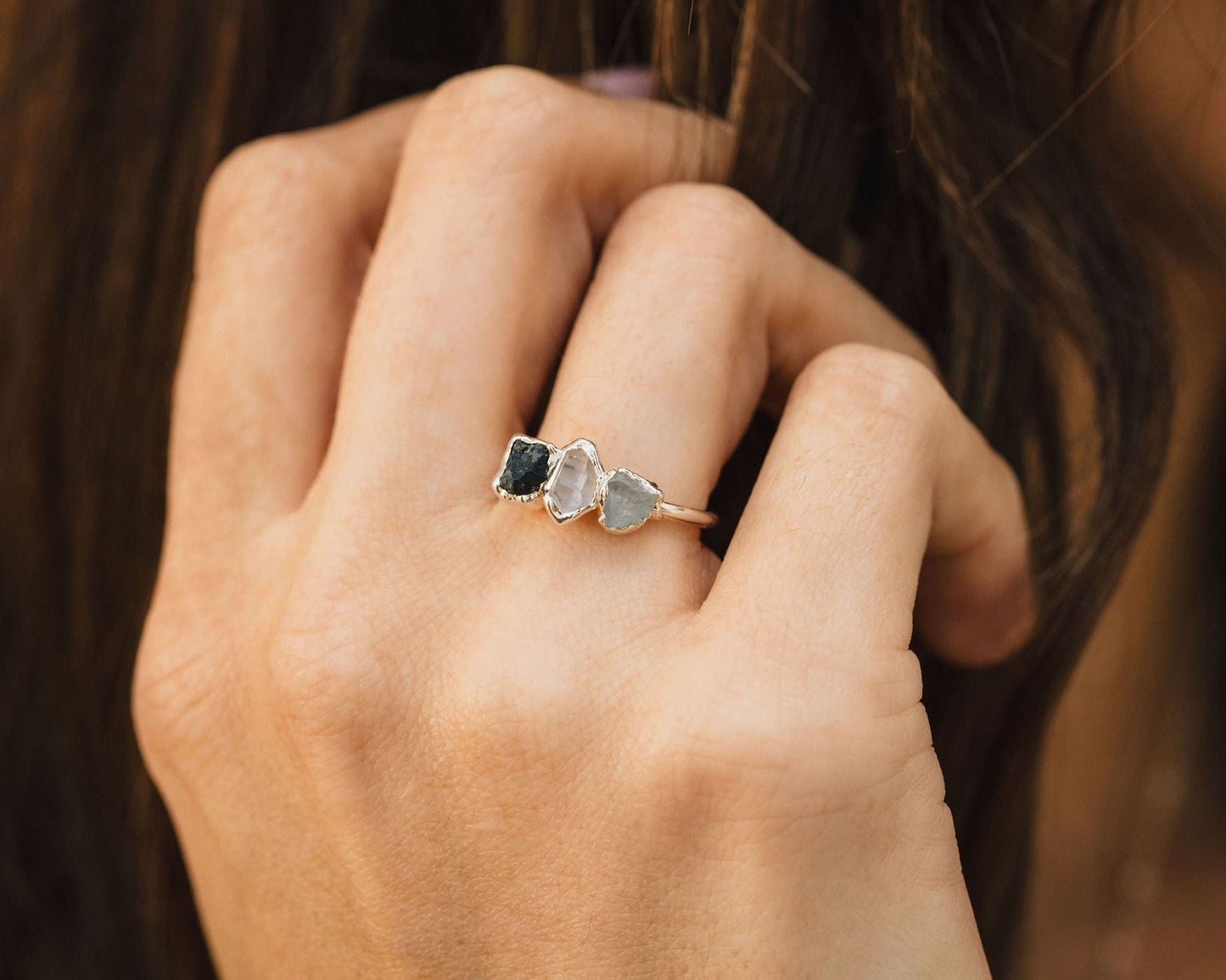 A close-up of a person's hand wearing a ring with three gemstones.