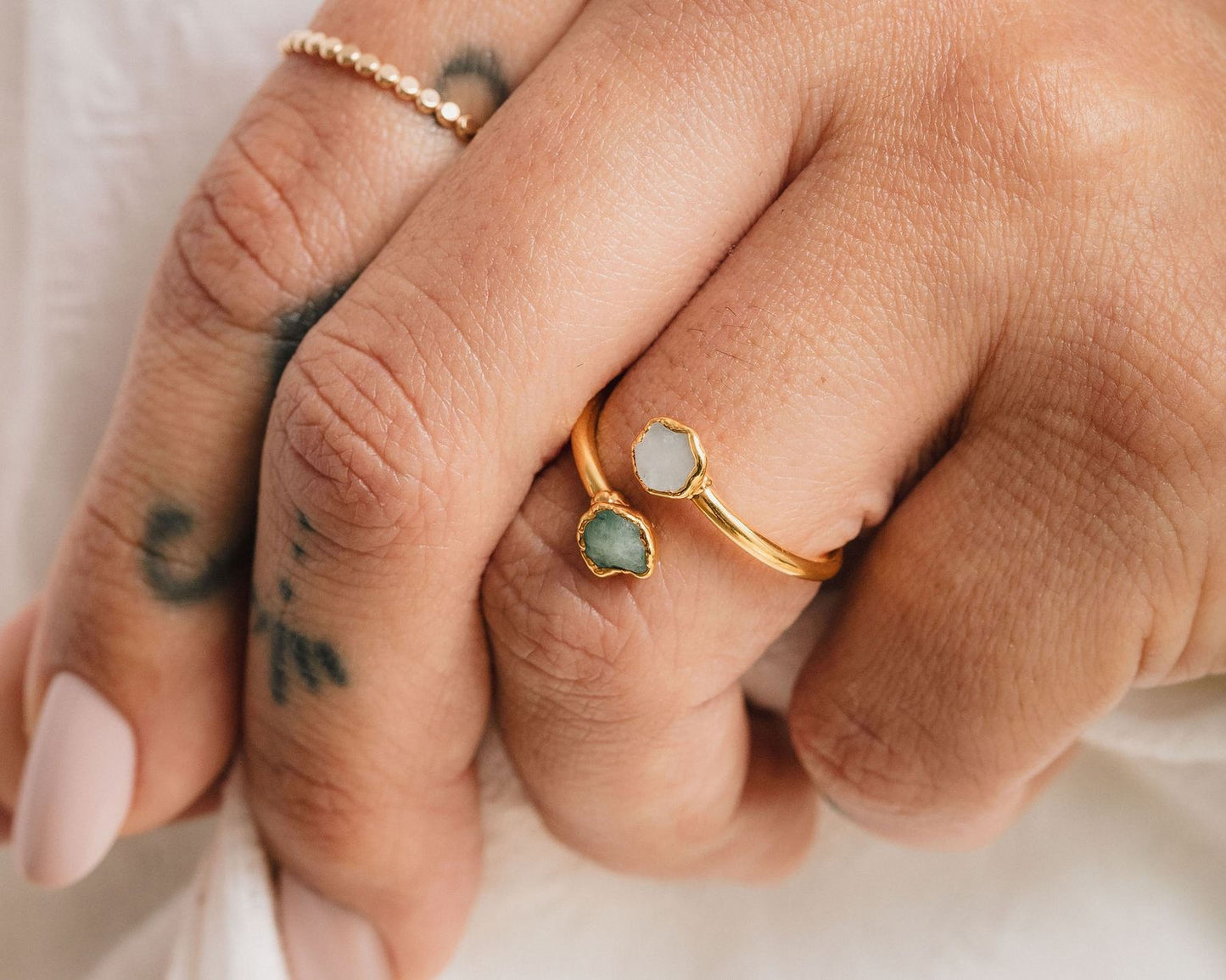 A close-up of a person's hand wearing two rings, one with a green gemstone and the other with a white gemstone.